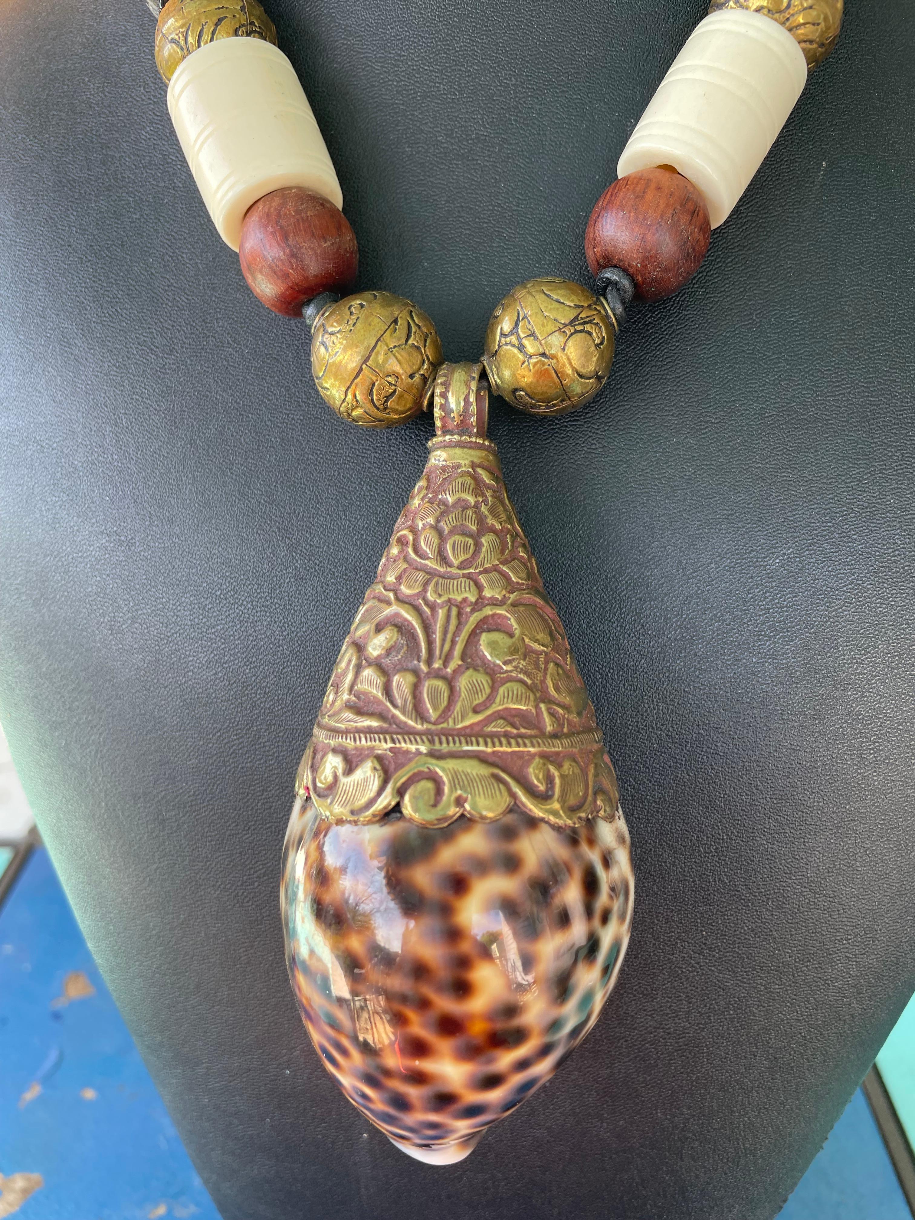 Lorraine’s Bijoux offers a Large Spotted Tiger Cowrie shell from Tibet with brass Repousse work pendant . This a handmade and One of a Kind, gorgeous piece. The magnificent shell is enhanced with large Tibetan brass beads, Bone barrel beads,