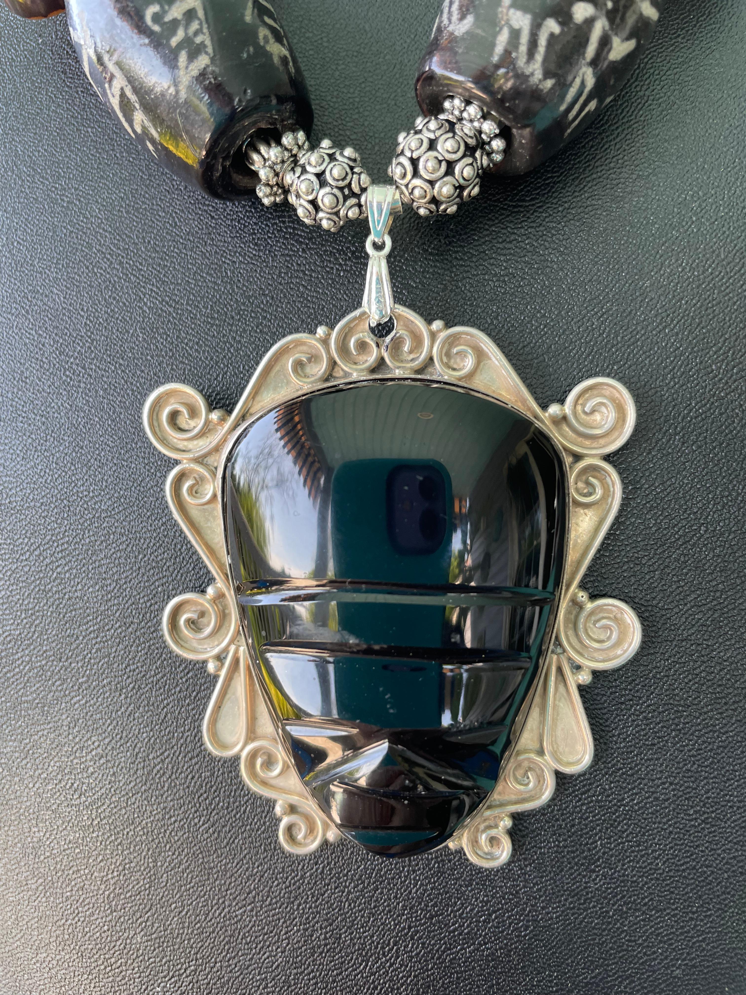 Lorraines' Bijoux propone una grande collana con ciondolo a forma di maschera messicana in argento e onice. Meravigliosi vetri africani, fette di noci esotiche, perline in legno e resina, ossa intagliate, turchesi Kingman, perline d'argento