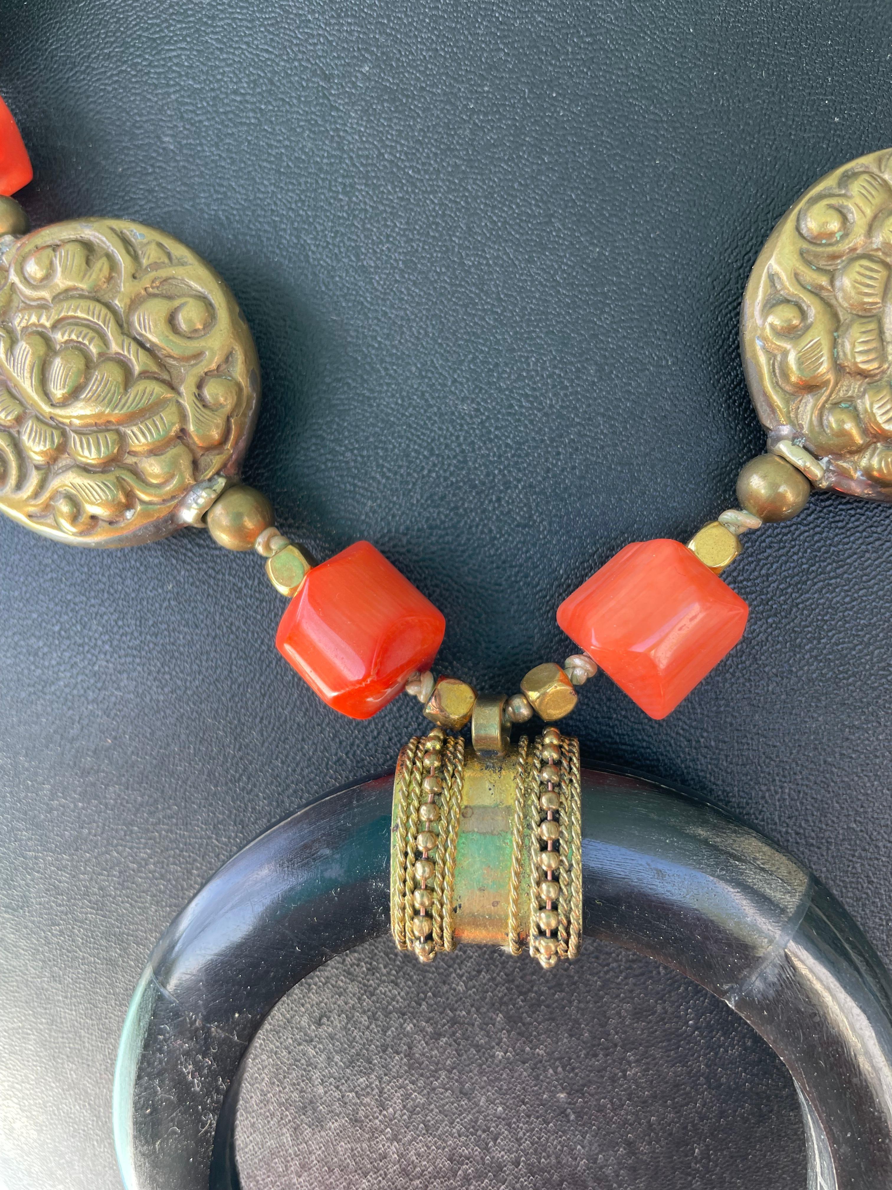 Lorraine’s Bijoux offers a handmade vintage Bone African Naja pendant with brass trim necklace.Large Tibetan Brass Repousse beads, faceted orange coral,
Tibetan Carnelian inlaid beads, and large curved Bone neckpieces, and wooden beads finish this