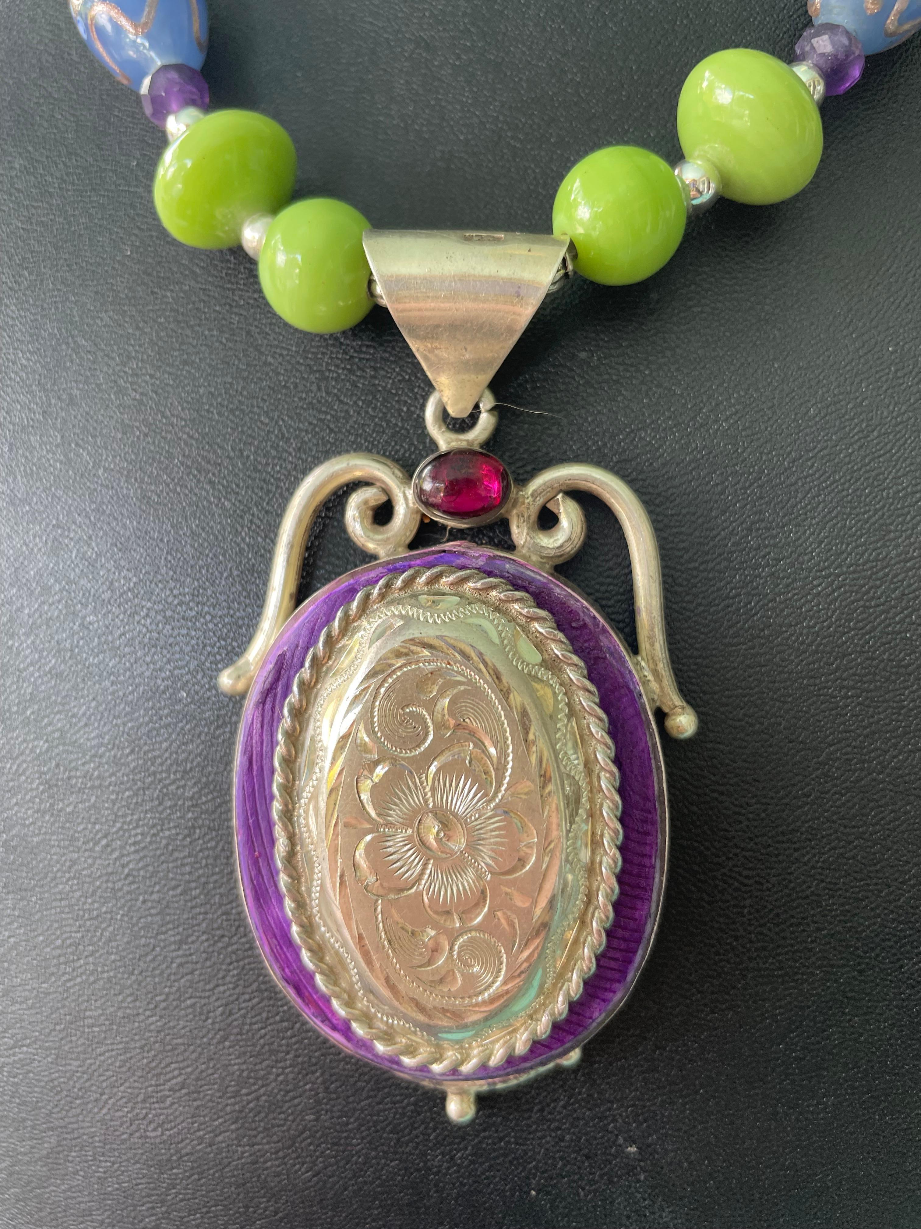 Lorrain's Bijoux bietet einen Anhänger aus balinesischem Sterlingsilber im Vintage-Stil mit einer Concha aus amerikanischem Südwest-Sterling als Herzstück (ebenfalls mit einem Granat in Cabochon-Fassung) an.
Eine Kette aus venezianischen Glasperlen