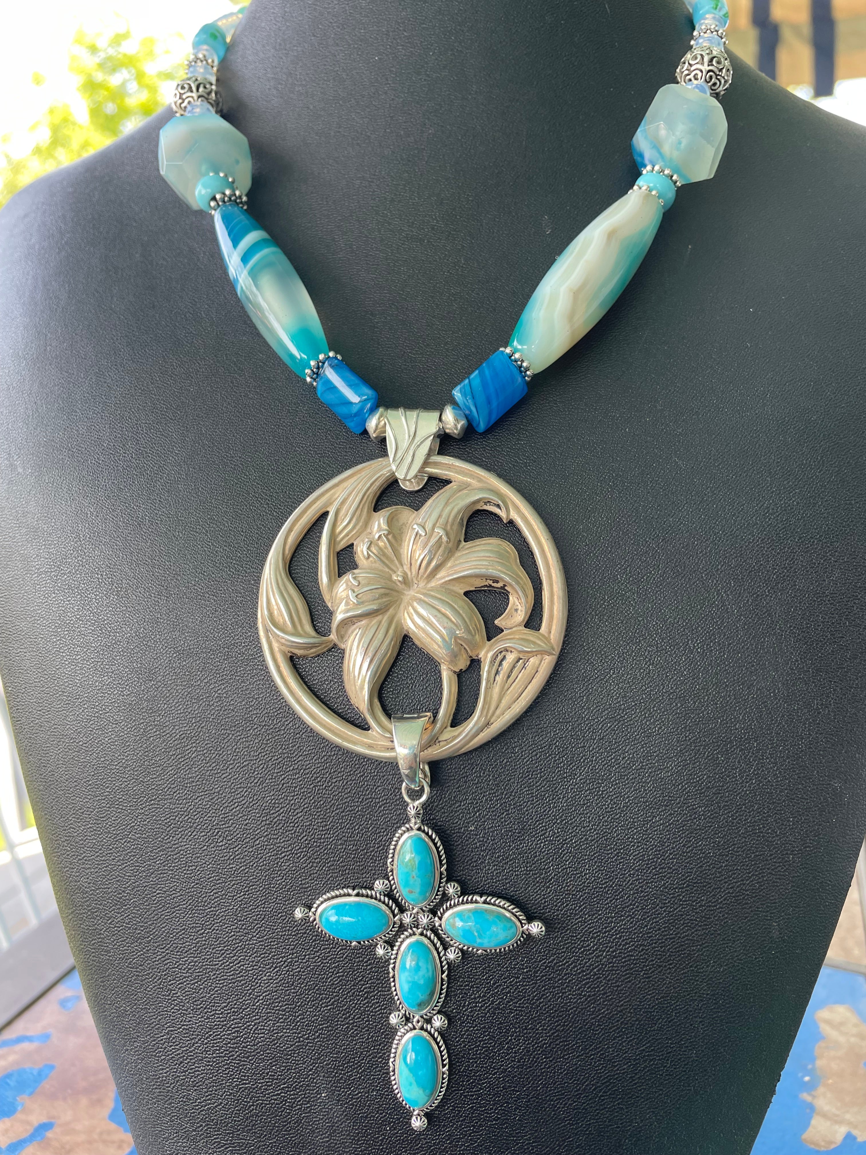 Lorraines' Bijoux offre una spilla a forma di giglio d'epoca in argento sterling e una collana d'epoca in turchese nativo americano e ciondolo a forma di croce in sterling. 
Agate blu e perline di vetro vintage aggiungono un tocco di blu all'insieme