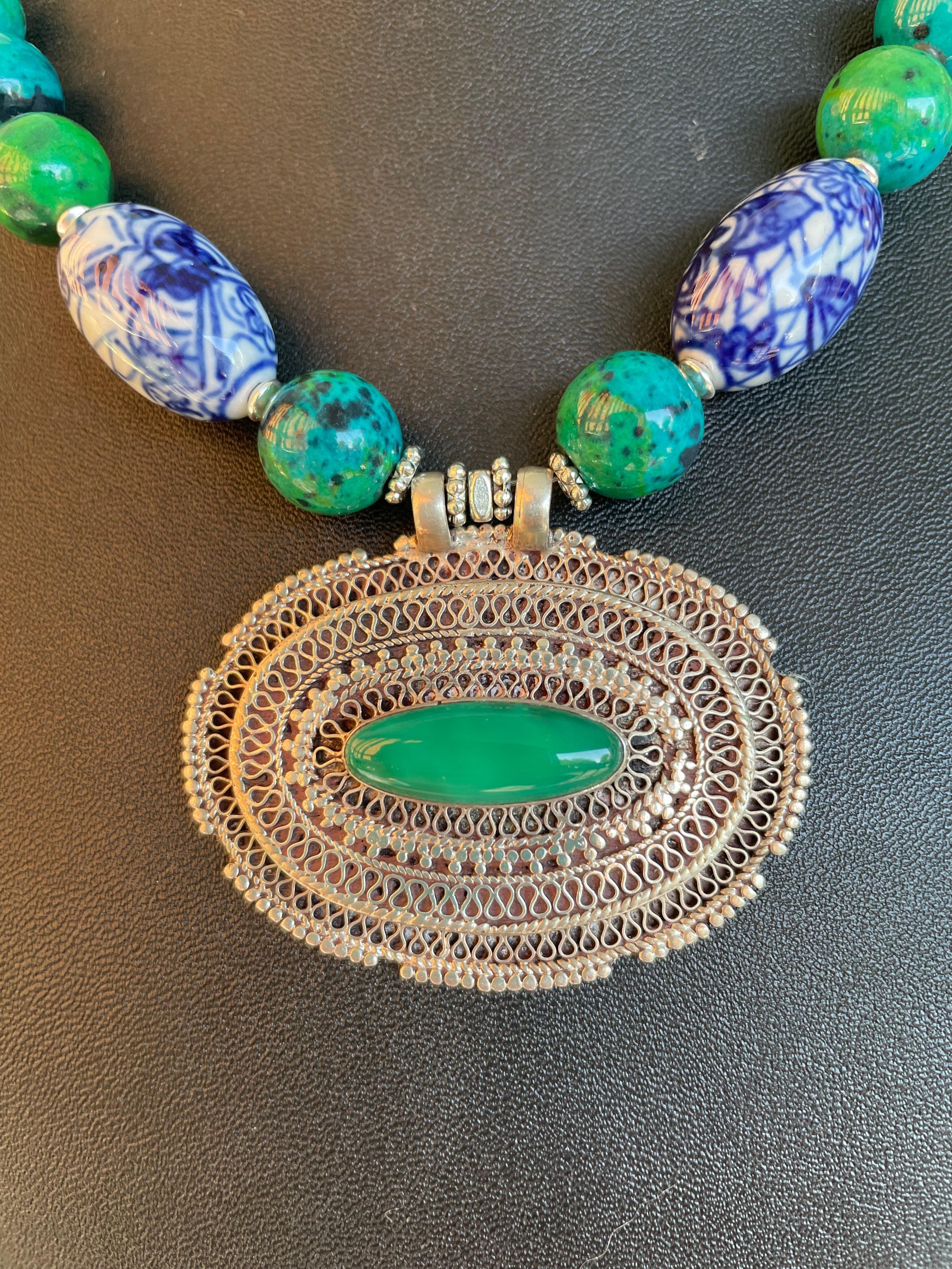 Lorraine’s Bijoux offers a one of a kind Vintage Tibetan,(Silver and glass) pendant handmade necklace. This hand wrought centerpiece is stunning and is enhanced by the large Azurite ,blue green beads and the hand painted Chinese Porcelain accent