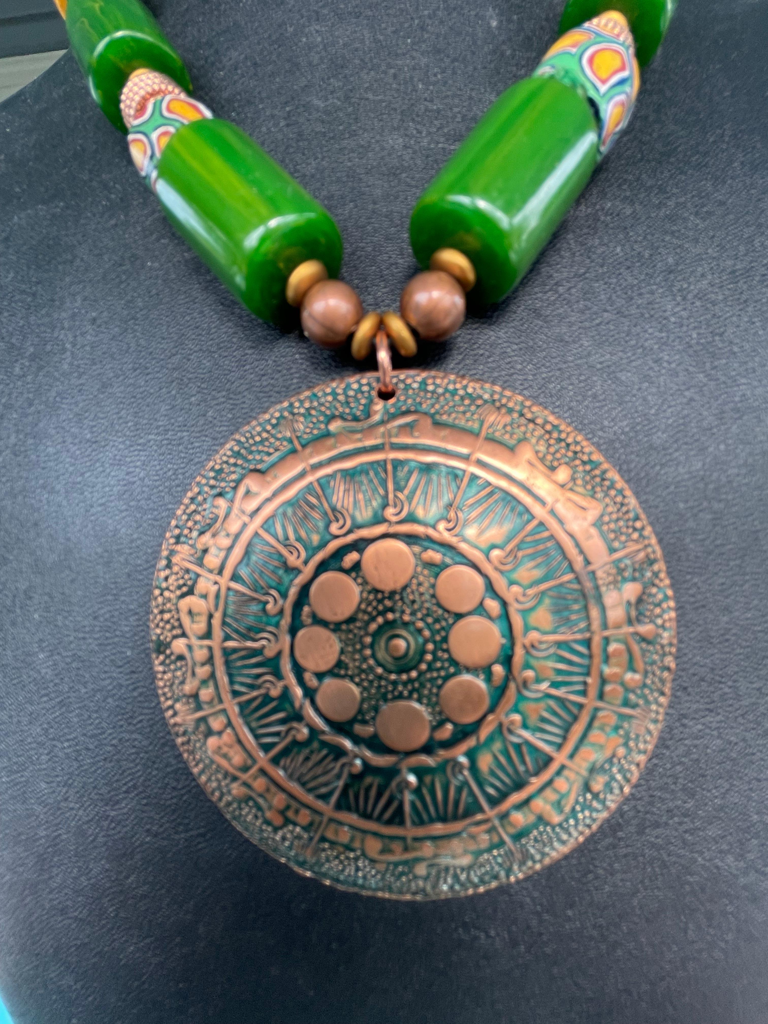 Lorraine’s Bijoux offers a Large Vintage Copper Deco Pendant Stunning Necklace.This one of a kind, handmade, piece consists of a repousse copper tribal pendant that is beautifully enhanced by Vintage dark Green Bakelite tubular beads and clasp,