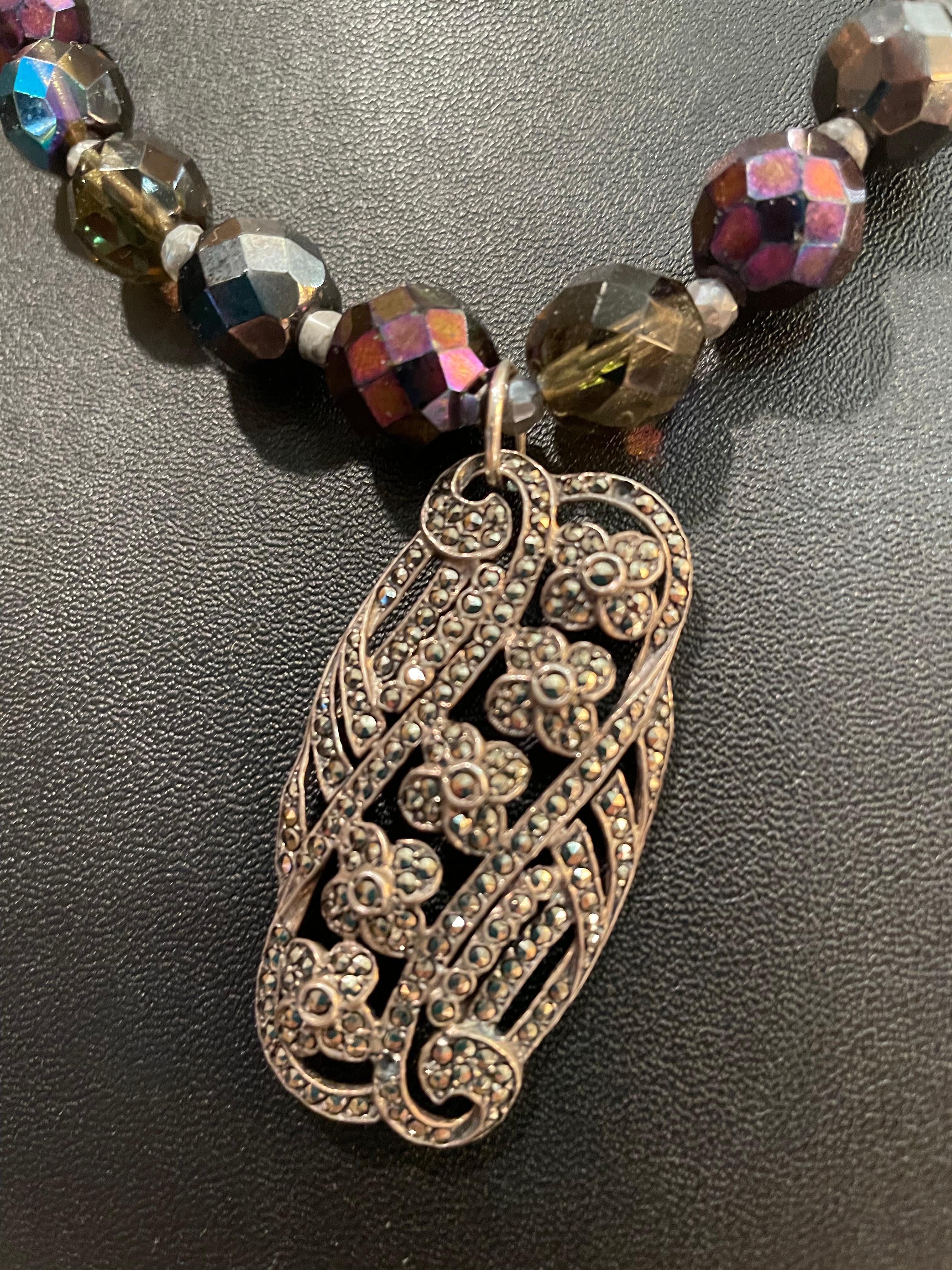 Lorraine’s Bijoux offers a Stunning necklace with a vintage sterling Silver and Marcasite Brooch Pendant and large Purple Aurora Borealis Czech crystal beads. This gorgeous piece will enhance any outfit, from a pair of jeans to an evening