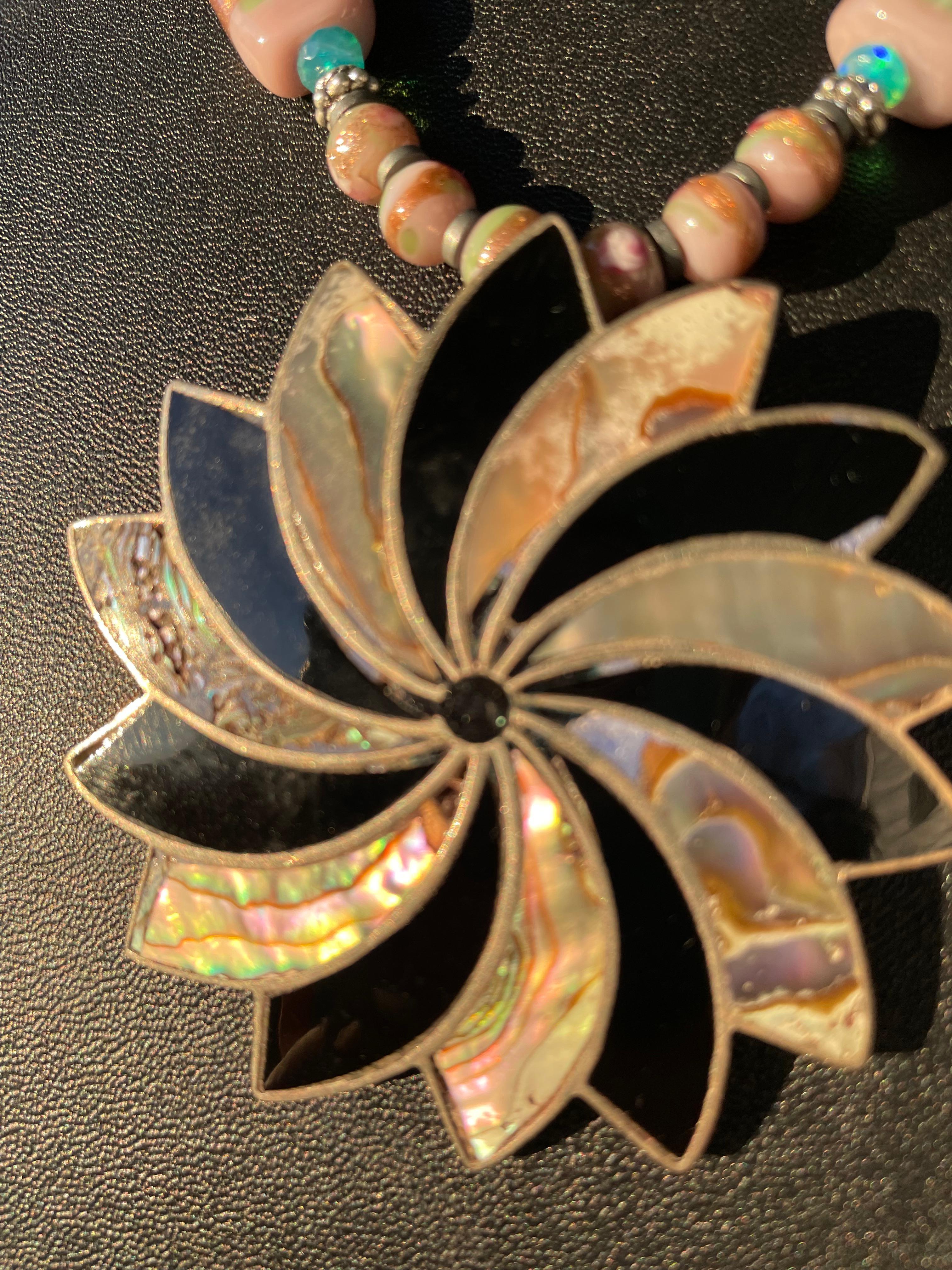 Lorraine’s Bijoux offers a Vintage Mexican,
Onyx,Sterling Silver, and Paua shell, mid 20th century pinwheel shape pendant necklace. This piece is stunning and very dramatic and represents the spinning of the wheel of life. Enhancing this amazing