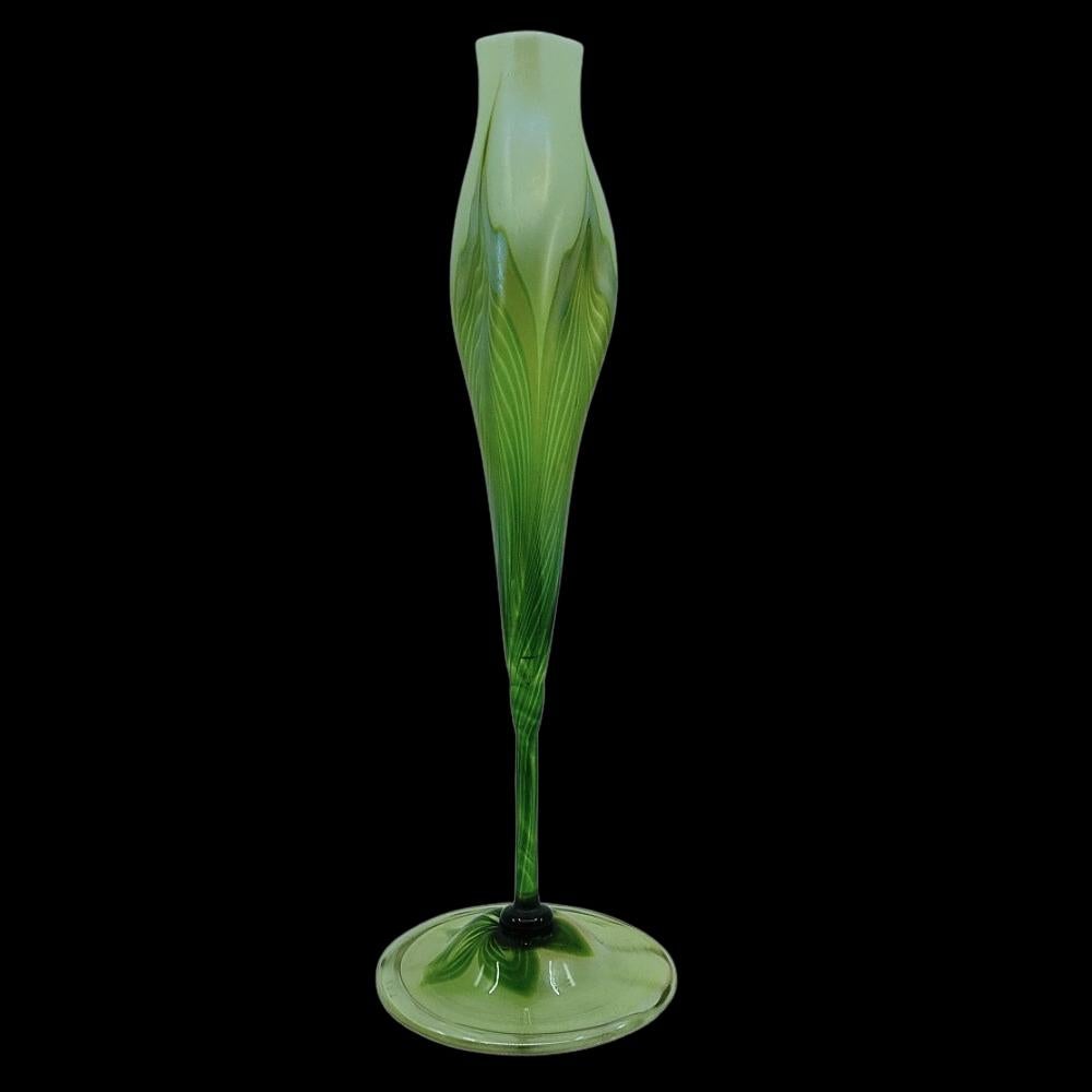 Offering this beautiful, decorated Louis Comfort Tiffany favrile art glass floriform vase with green feather and white opal decoration. This floriform vase features a long stem body with tri-lobed mouth and decorated clear applied foot. Signed on
