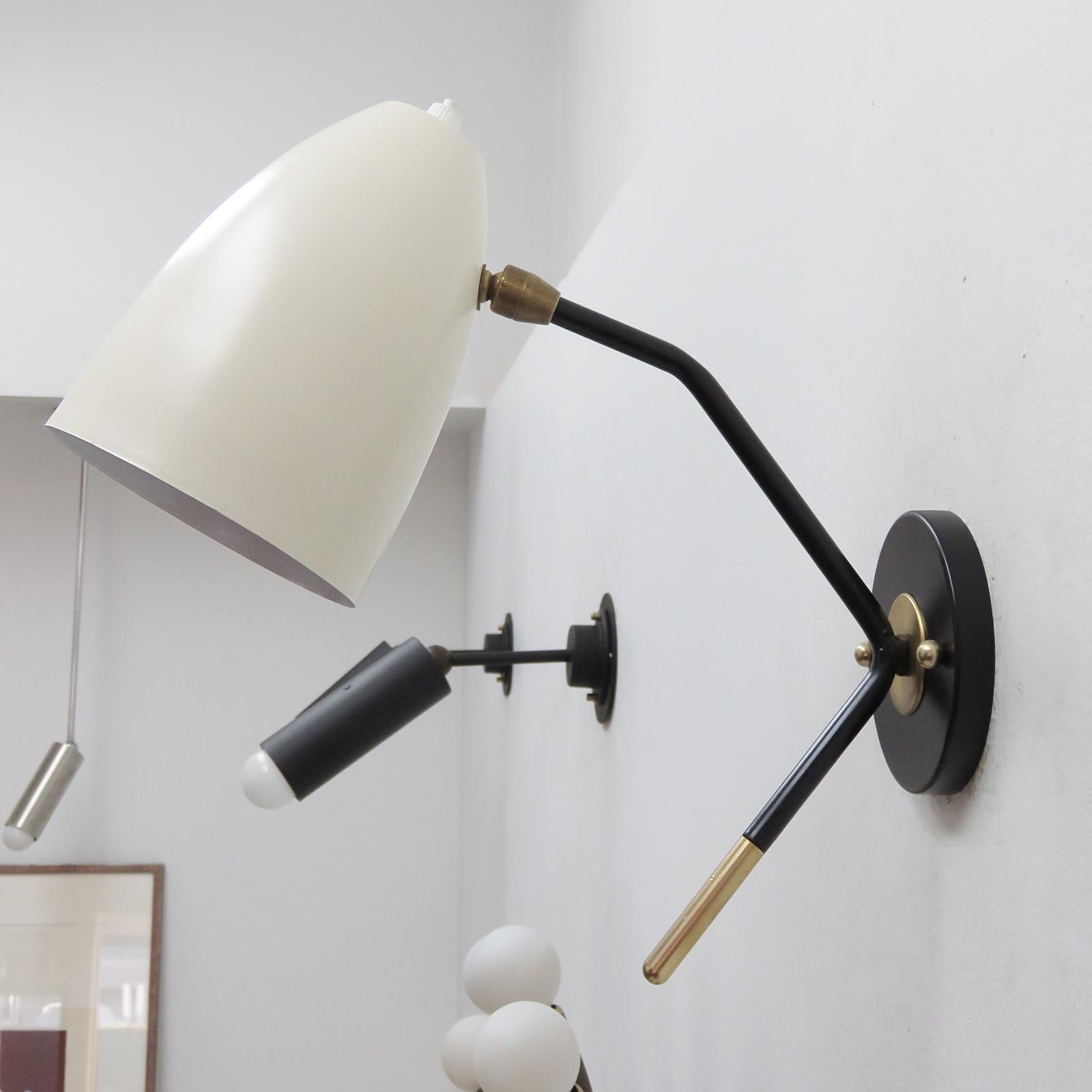 Wonderful two-tone LE-1 wall lights with fully adjustable two tone brass shades (egg shell with white enameled interiors) on black enameled arms with decorative brass tips, each shade has an individual on and off switch. One E26 socket per fixture,