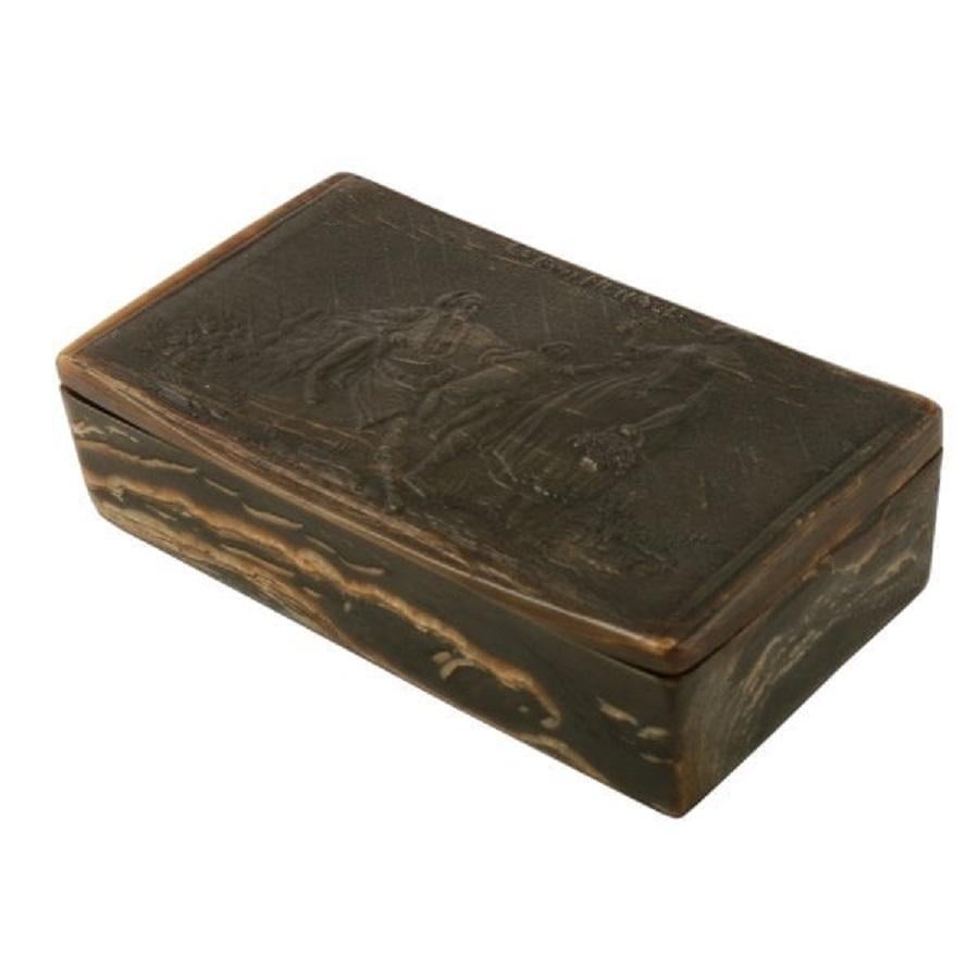 A late 18th to early 19th century horn snuff box.

The box has a hinged lid that has a scene of a lady with a basket of grapes next to a Gentleman with a child on his knee.

Above them are the words 