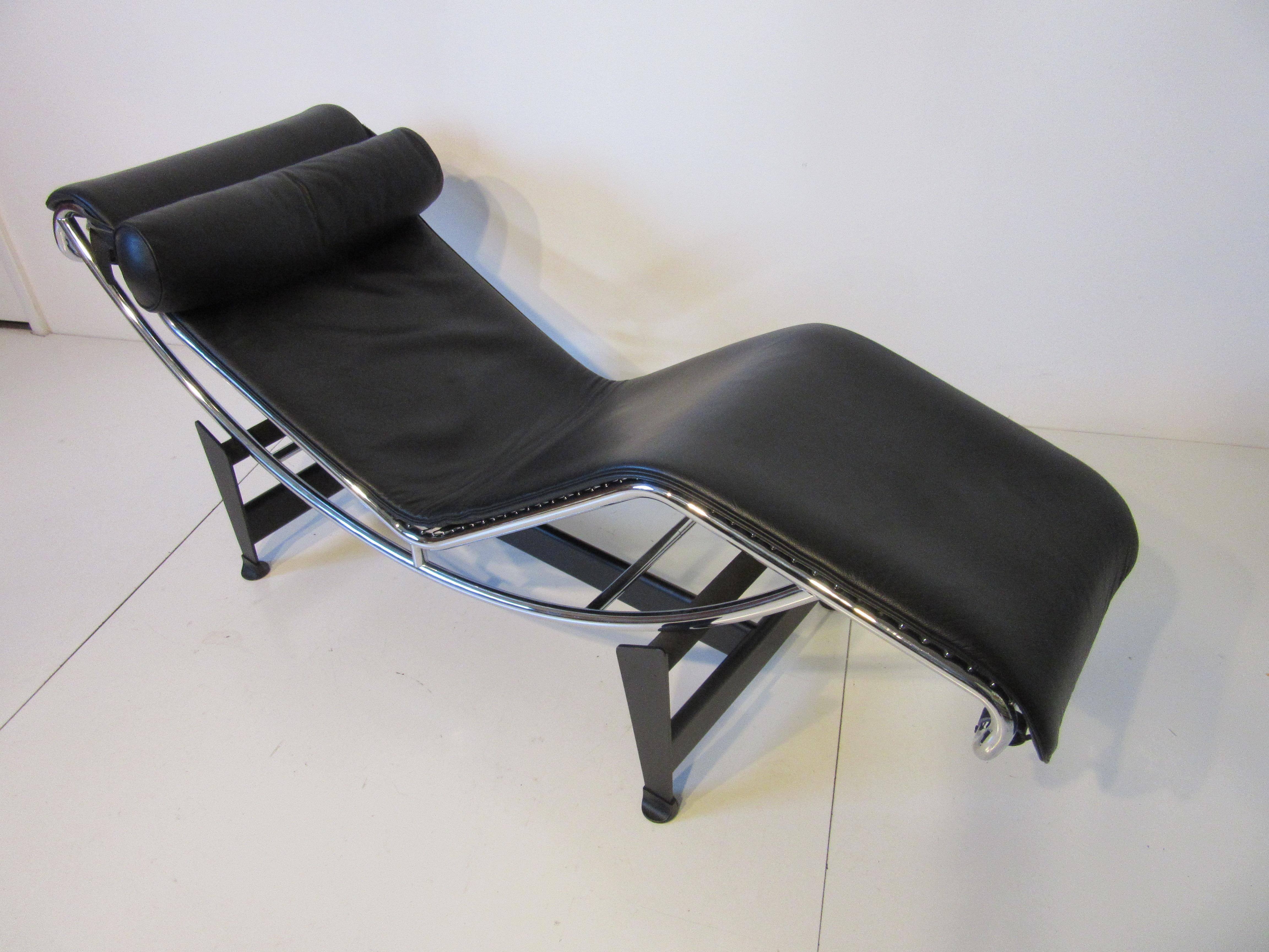 A Iconic two-piece LC-4 lounger with soft black leather pad and head pillow with chrome frame , woven nylon straps sitting on a black metal base. The chair adjusts on it's base to any comfort level making it one of the best lounges ever designed.