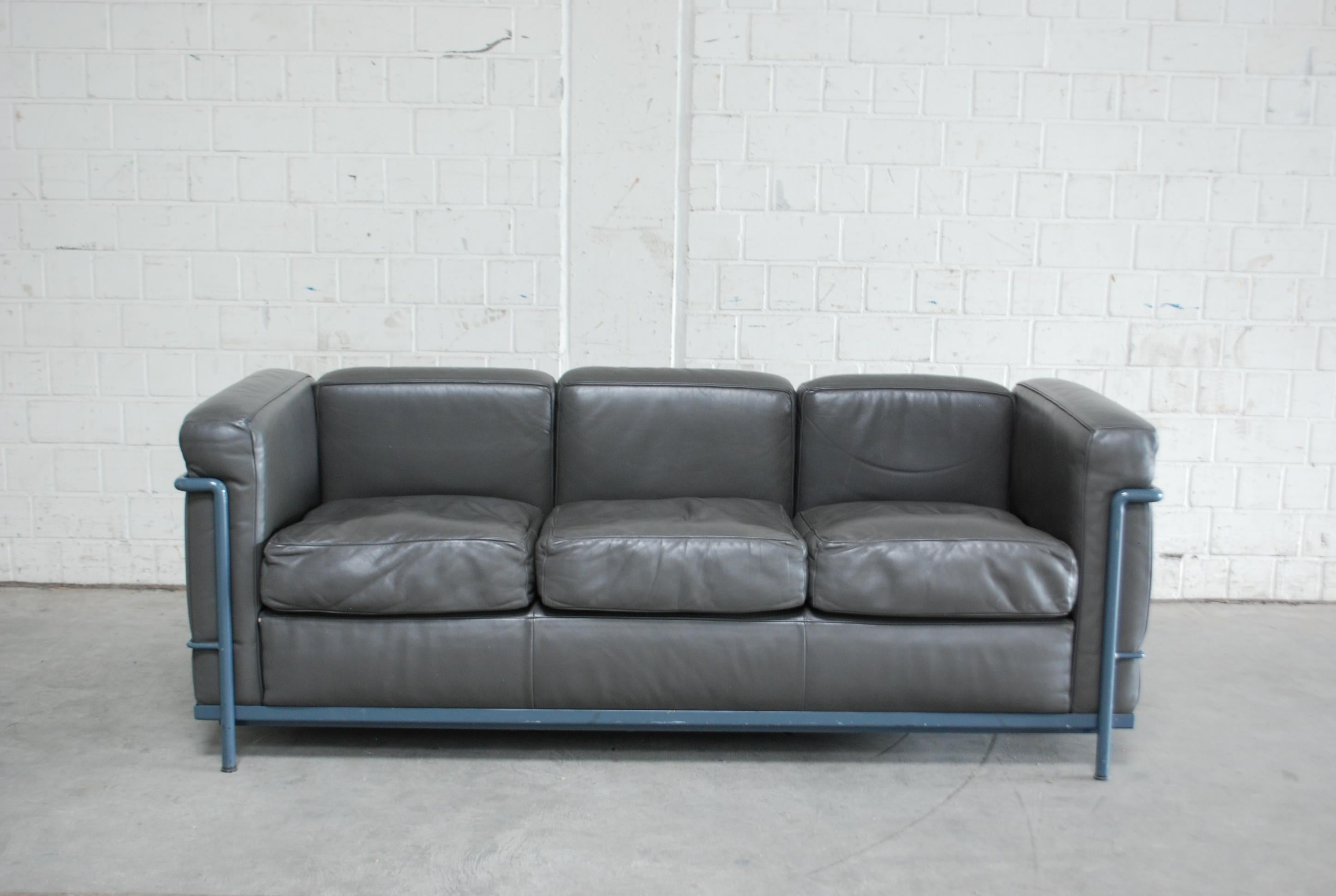 This LC2 three-seat sofa in grey leather was designed by Le Corbusier and produced by Cassina.
It features a blue/ grey colored tubular steel frame. Some marks on the tubular frame.