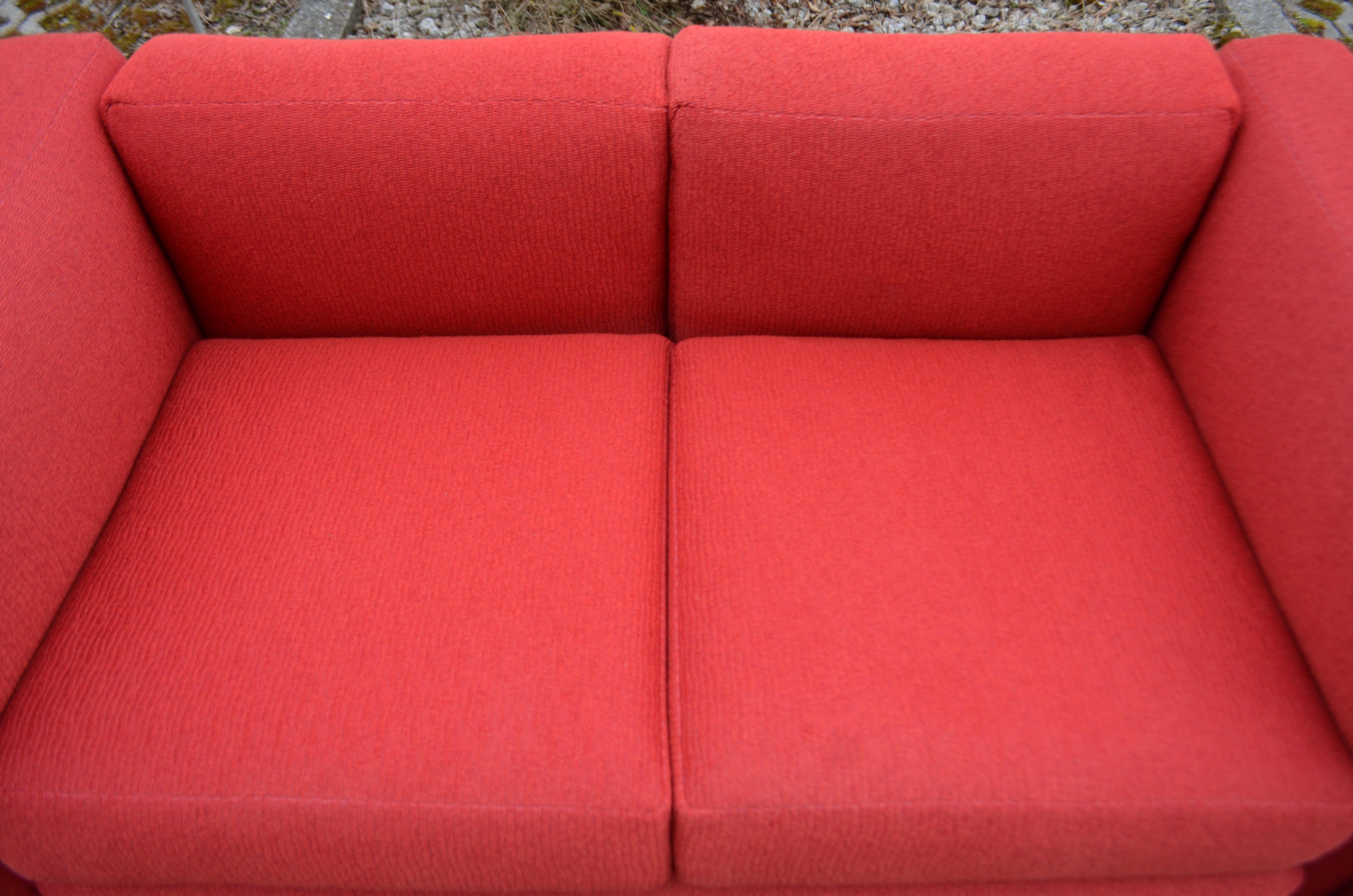 This LC2 two-seat sofa in red fabric was designed by Le Corbusier and produced by Cassina.
It features a classic chrome tubular steel frame. 
The fabric is a red structural luxury fabric and was covered some years ago.
Also the completely pillows