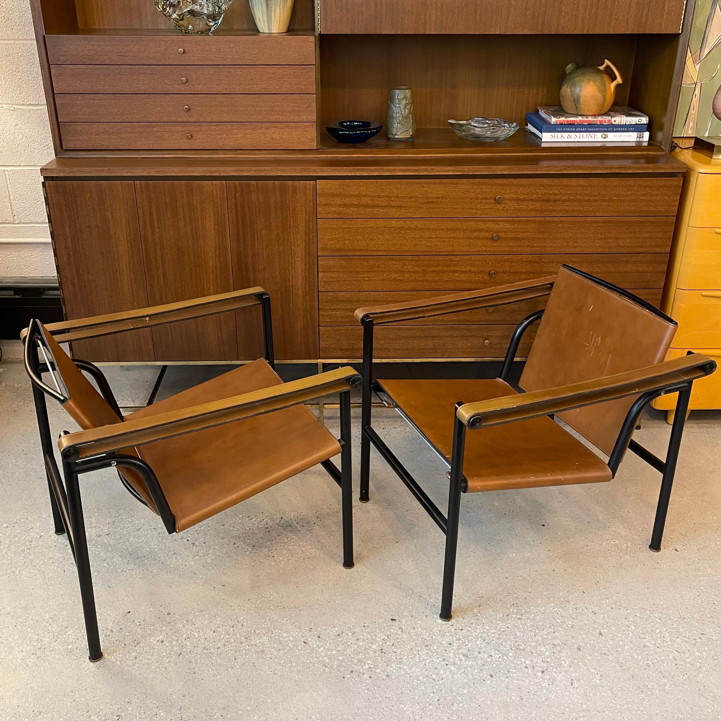 Pair of LC1, Basculant, sling armchairs designed by Le Corbusier, Pierre Jeanneret and Charlotte Perriand in 1928 and manufactured by Cassina, Italy in the 1970's. These iconic Bauhaus chairs feature low, sleek, black steel frames with luggage tan