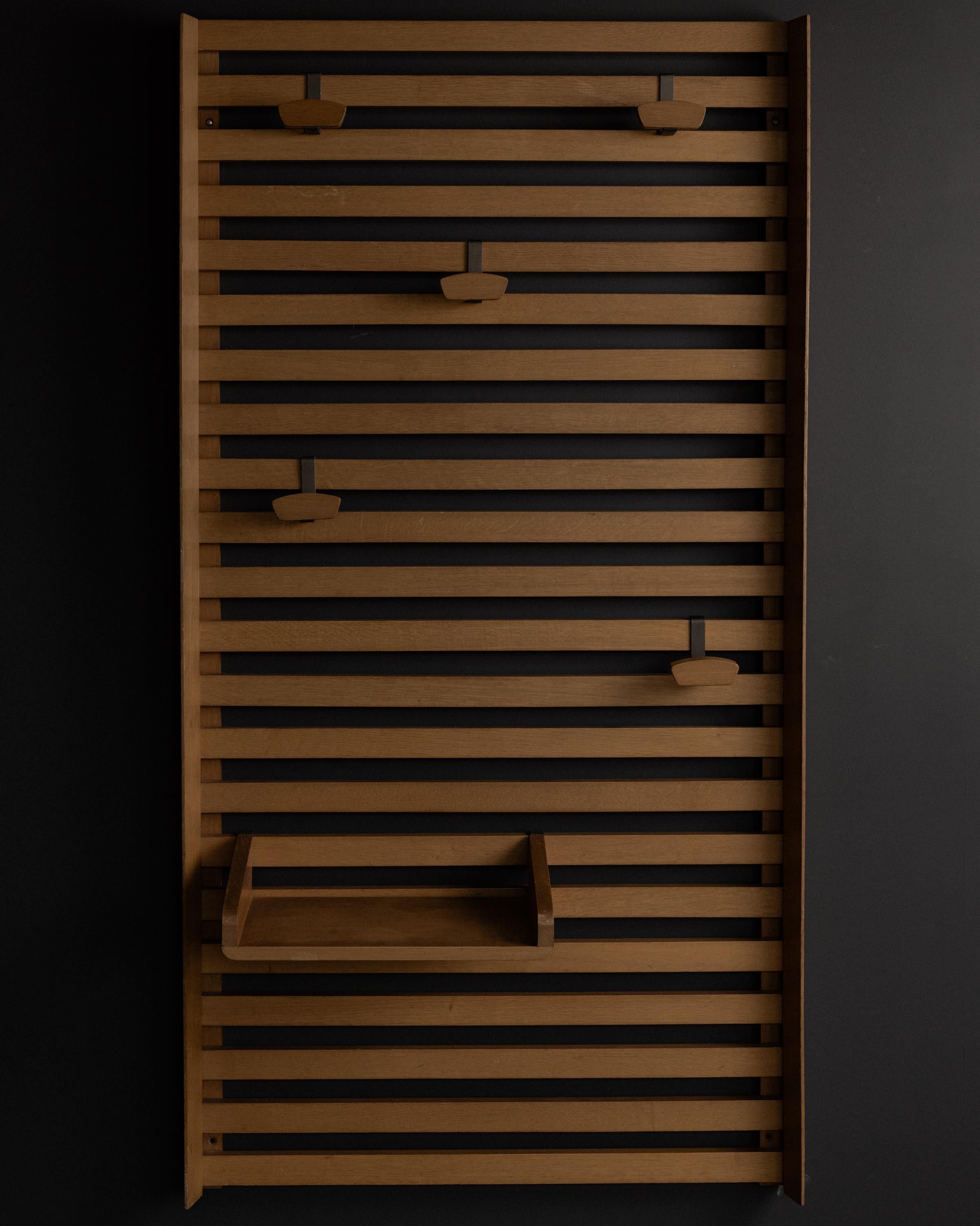 Wall-mounted coat rack designed by Le Corbusier for the Unité d'Habitation in Marseille, c. 1950s. Crafted from horizontal oak slats with five adjustable metal-and-wood peg hooks and a small integrated shelf. This piece exemplifies Le Corbusier’s