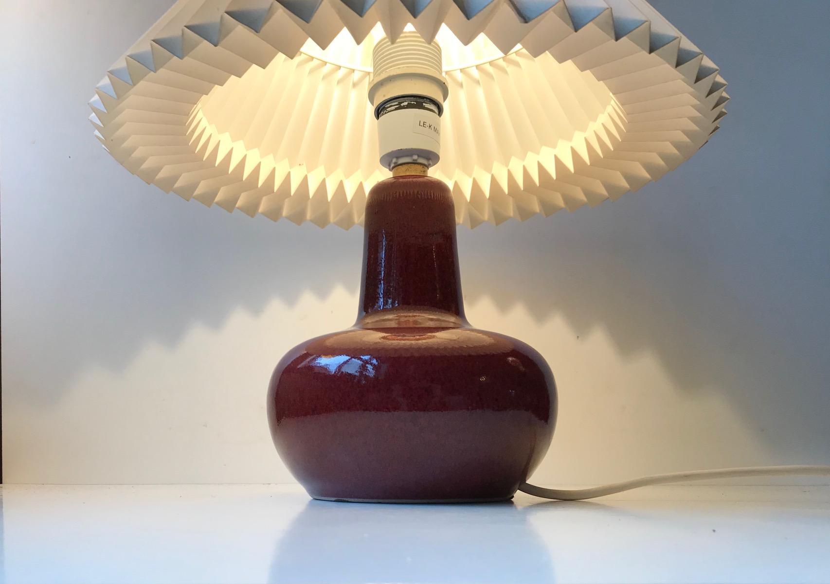 Vintage Danish Le Klint ceramic table lamp with deep and rich oxblood glaze. It was designed by Ole Bøgild in the 1970s. Stamped with both maker marks and designer attribution to the base. The table lamp is in excellent condition, without any