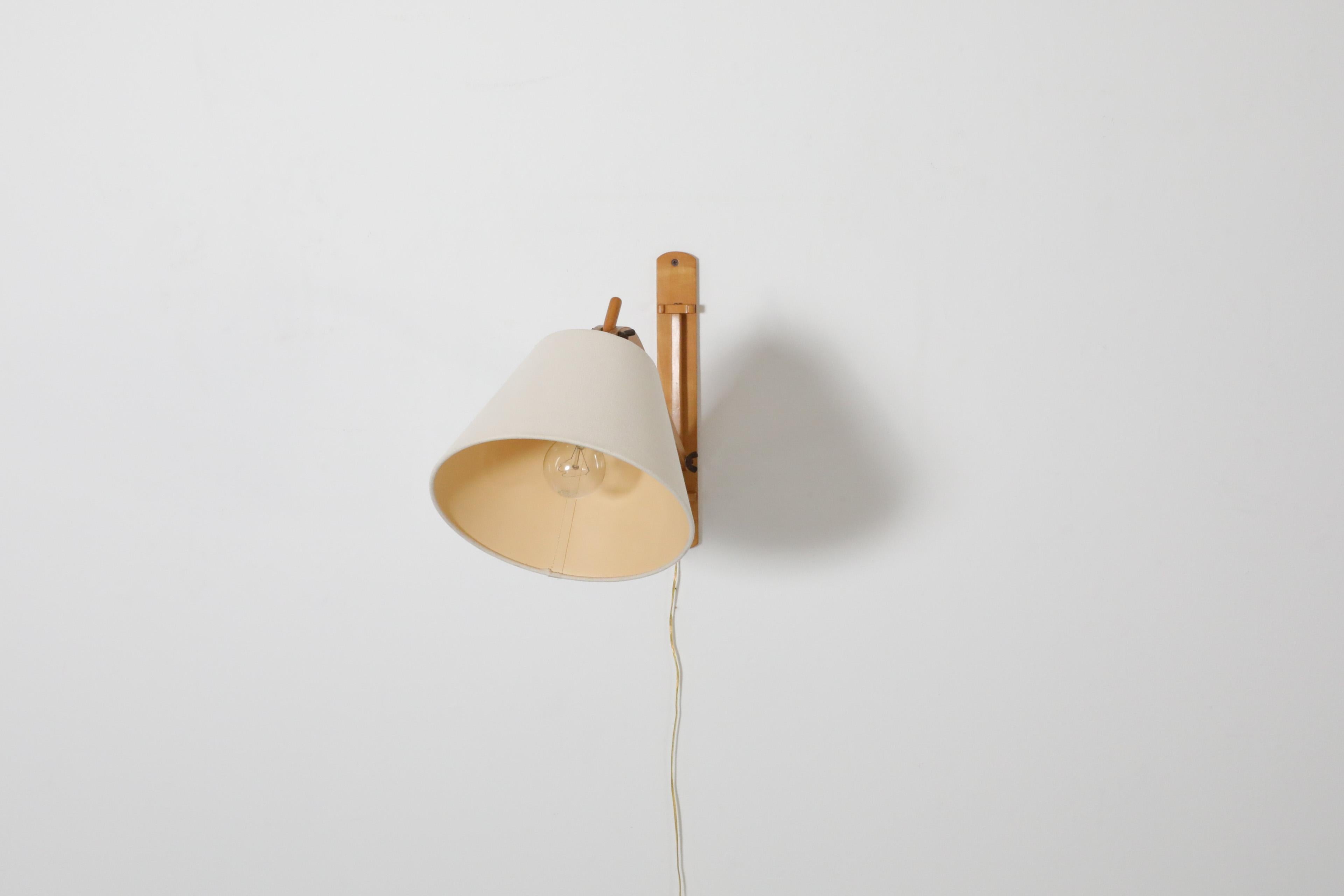 Mid-Century, Le Klint style, adjustable wall lamp in blonde wood with fabric shade. A cute light weight wall mount lamp with bent wood frame and metal accents. Lightly refinished, in otherwise good original condition with wear consistent with its