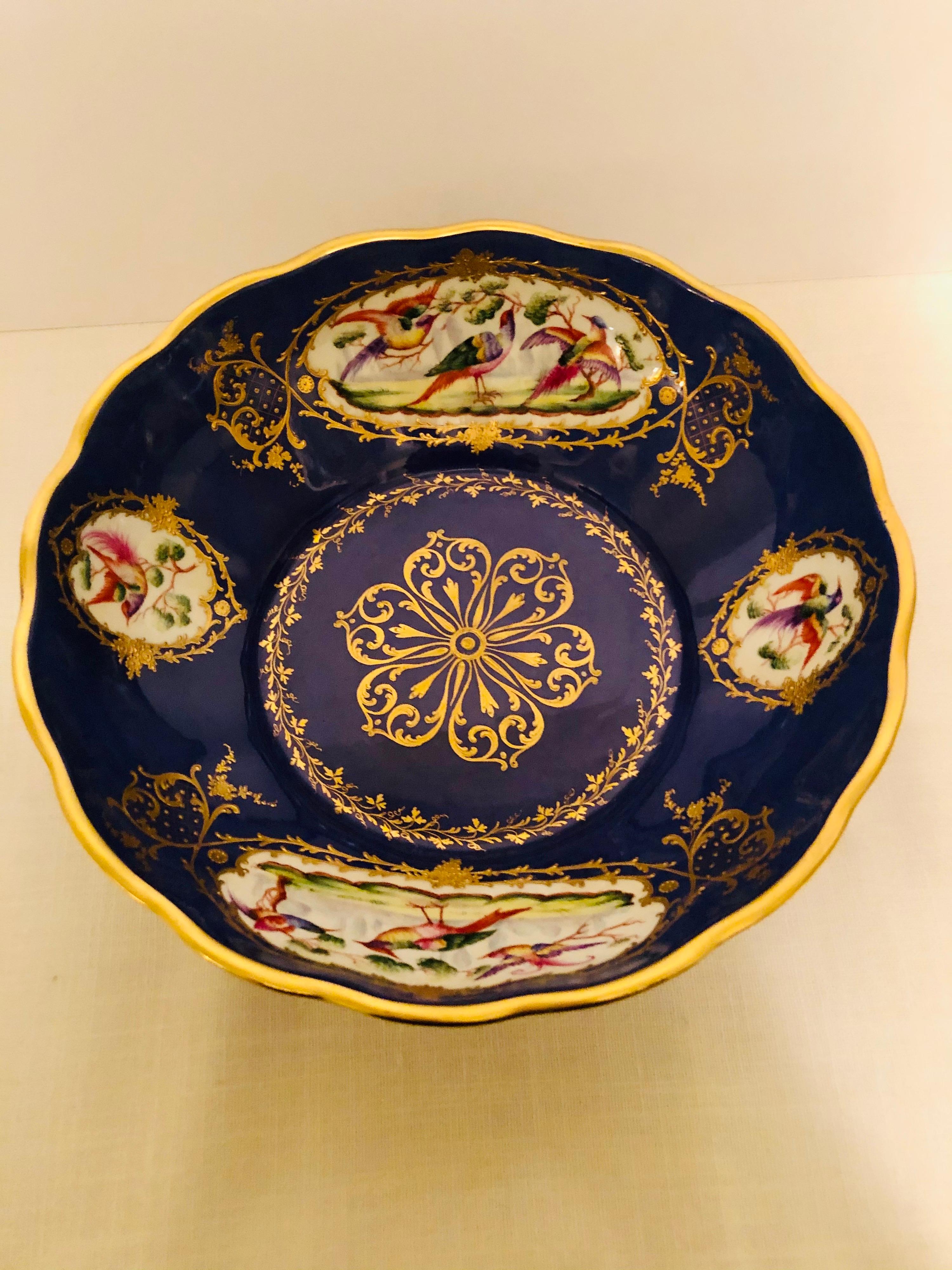 This is a gorgeous Le Tallec royal blue bowl with four cartouches of colorful exotic birds accented with raised gilding embellishments and raised gold jewel accents. This bowl has a gold center medallion, which has gold jewel accents. There are also