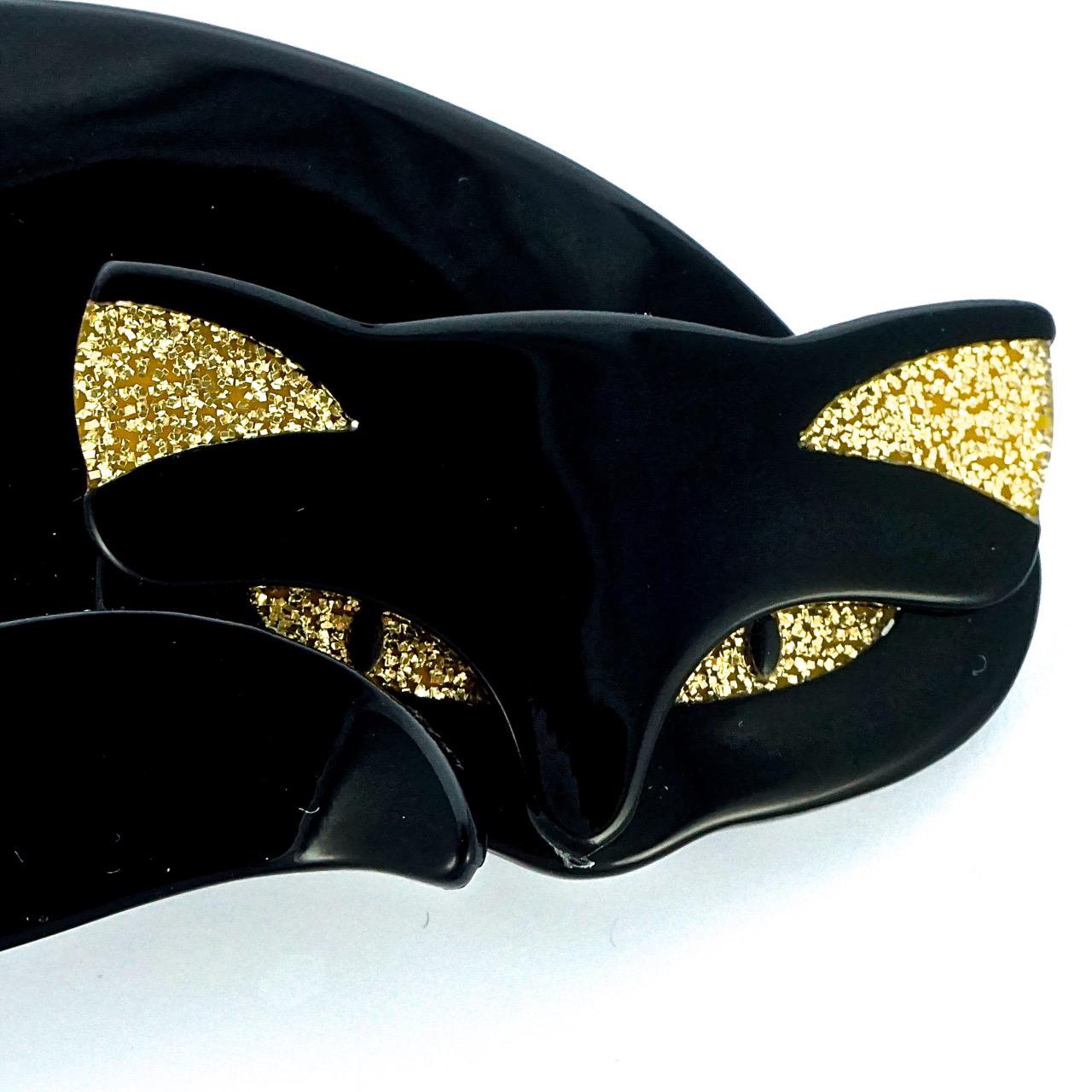 Lea Stein black Mistigri cat brooch, with gold sparkly eyes and ears. The brooch is made from layered plastic, and measures a maximum of 8.9cm / 3.5 inches by 5.05cm / 1.98 inches.

This is a beautiful collectable Lea Stein cat brooch in a wonderful