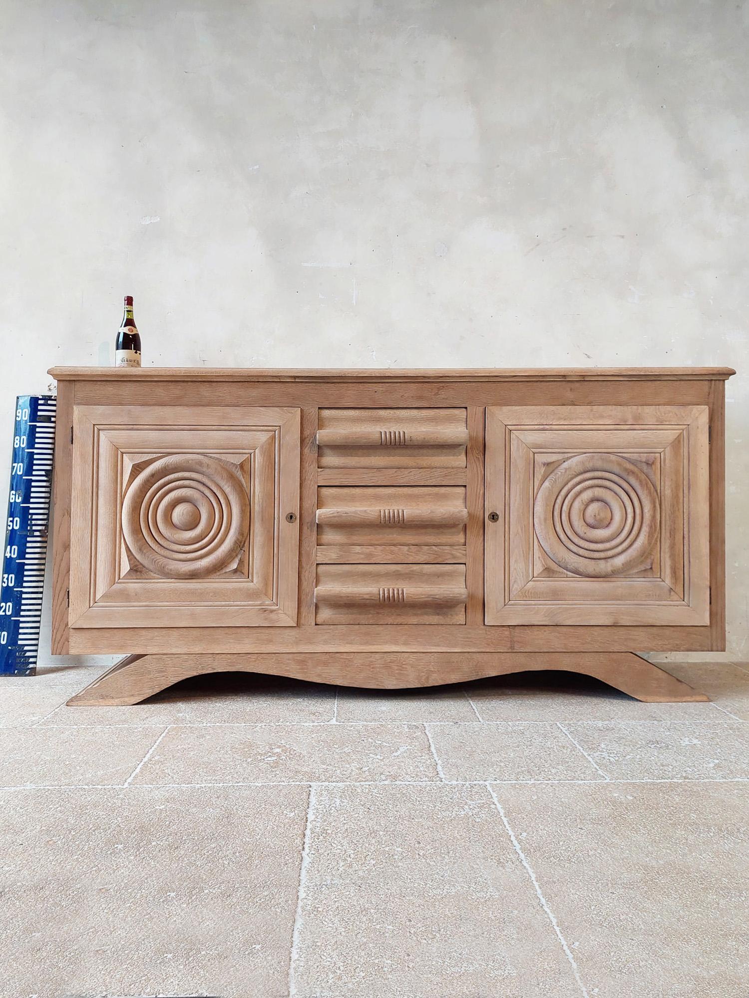 Leached oak sideboard by Charles Dudouyt from the 1940s, with two round paneled doors and 3 drawers with wooden handles that are incorporated within the design.

Measures: H 103 x W 204 x D 54 cm.
