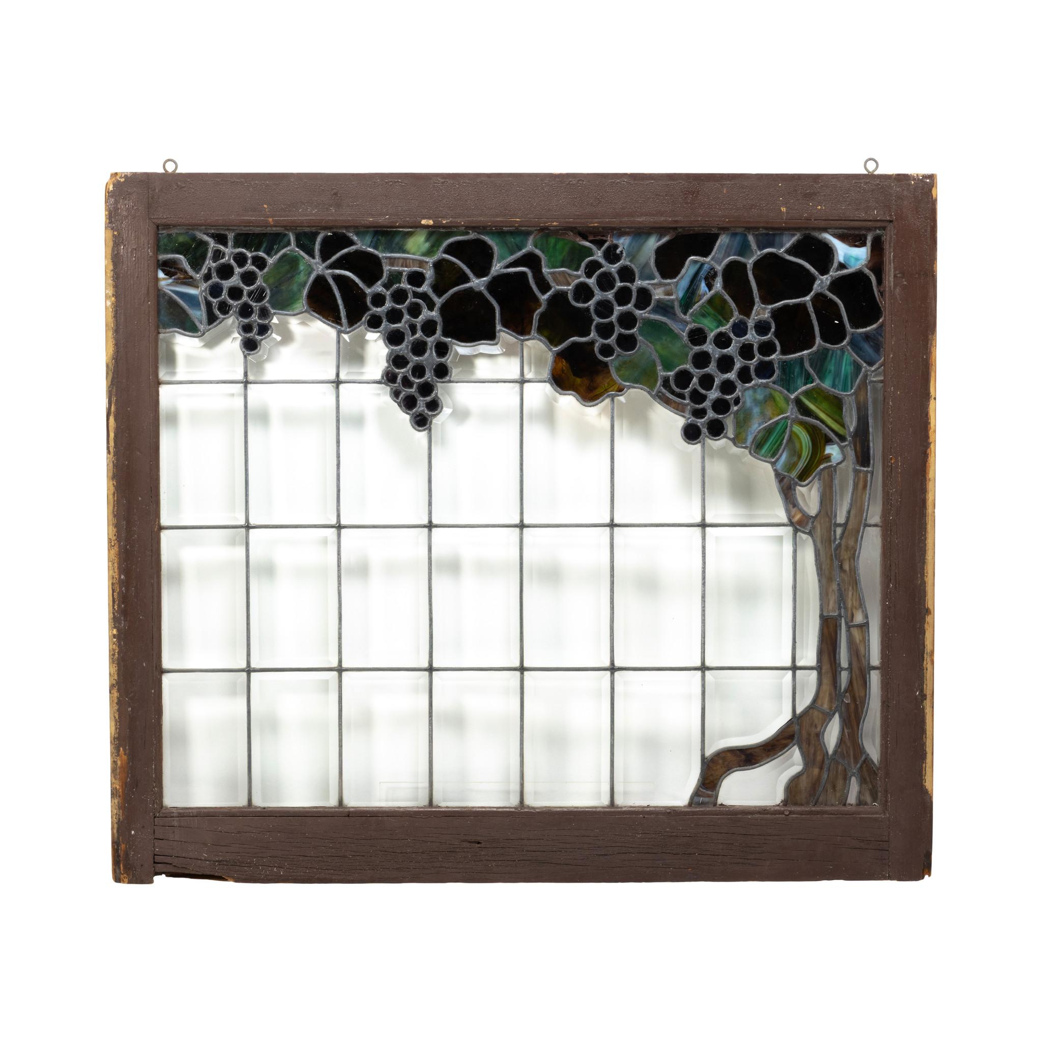 Ventana de cristal emplomado y biselado. Motivo de viñedo con vides trepando por el lado izquierdo de la ventana y uvas moradas cayendo en cascada desde arriba. Colores plomizos de morado, azul, marrón y verde. Treinta y dos cristales en total con