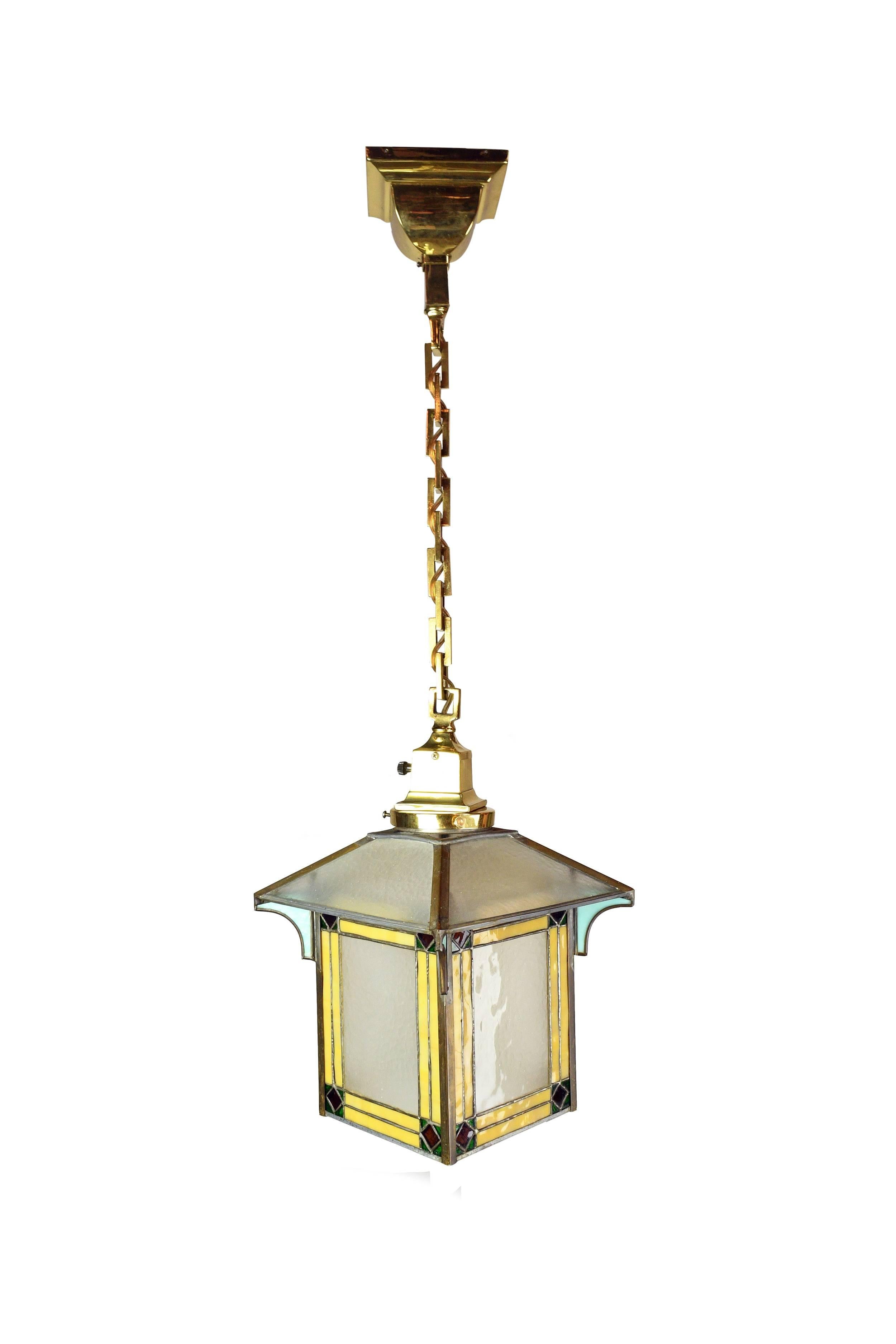 An adorable slag pendant, the shade of which consists of small pieces of multicolored leaded glass. On each corner of the shade, there is a piece of gorgeous glass that's a very rarely seen soft blue color. The rest of the pendant is polished brass,