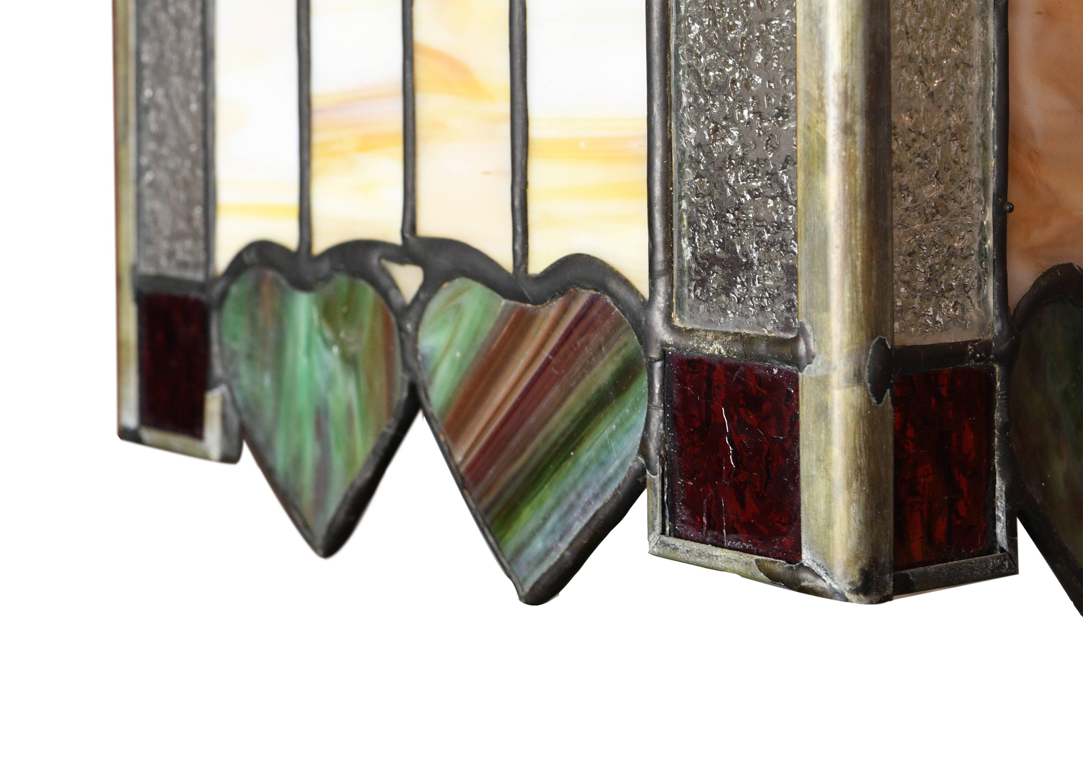 This pendant has heart-shaped patterns, which are unique and not often seen in lighting. The shade is made of small pieces of leaded glass, some in the shape of hearts, chevrons,and other geometric, multi-color designs. The warm tone of the fixture