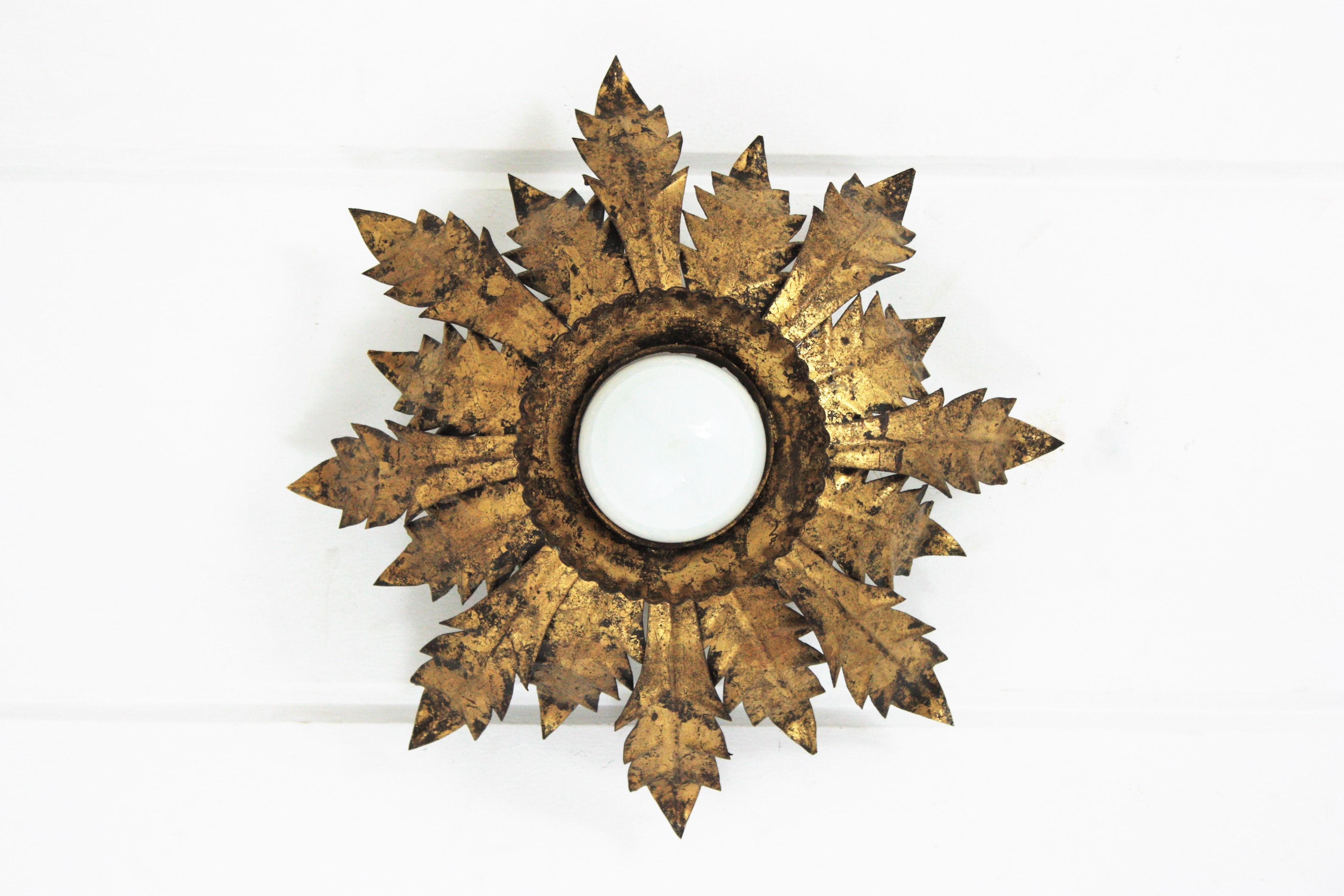 Sunburst flush mount light, metal, gold leaf, Spain, 1950s
This gorgeous spanish sunburst or crown ceiling lamp features alternating gold leaf gilt iron leaves surrounding a central exposed bulb. It has a terrific patina showing its original gold