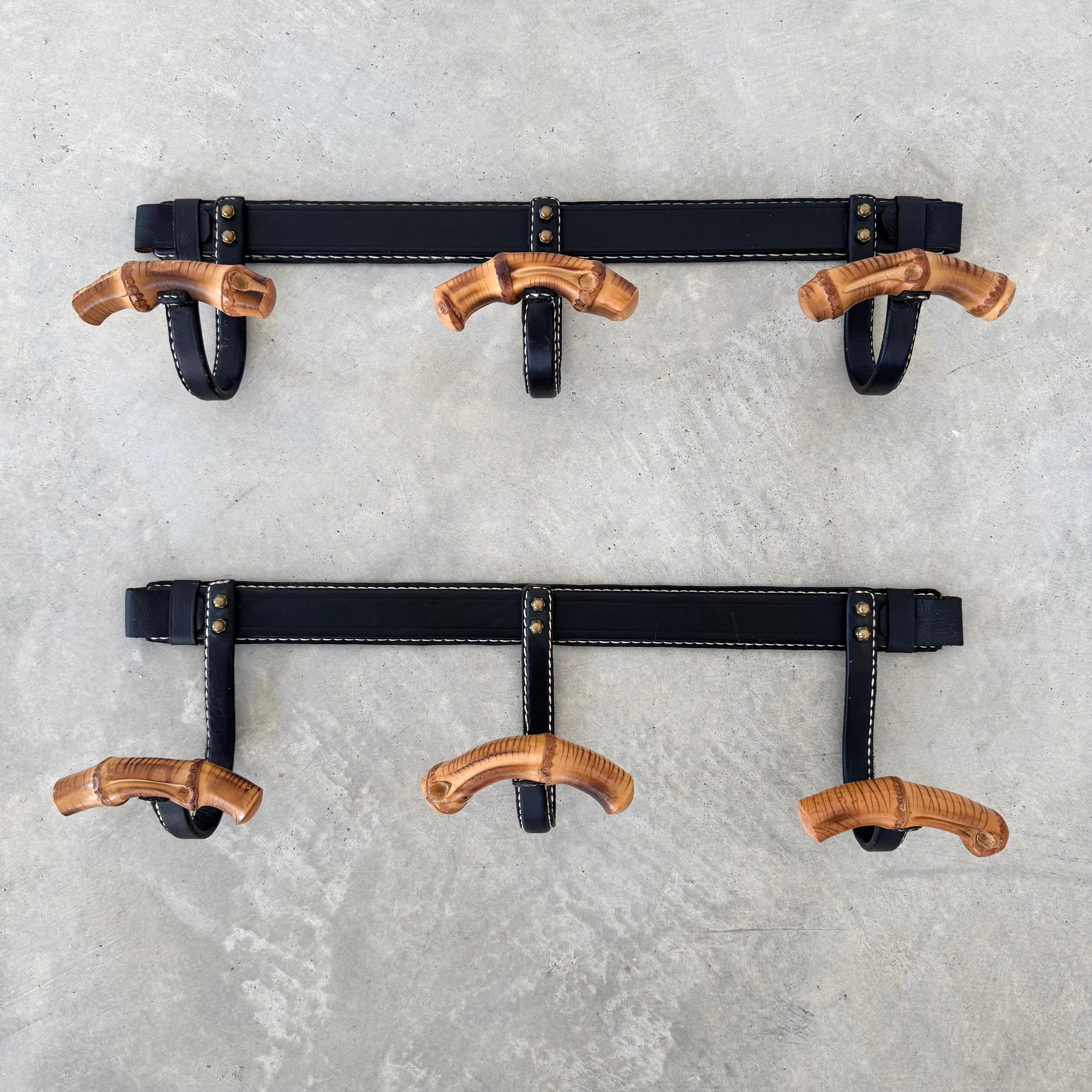 A gorgeous pair of coat racks by French designer Jacques Adnet. The black iron frames are completely wrapped in black leather, featuring Adnet's signature contrast stitching. Each hook is also wrapped in leather with a single piece of curved bamboo