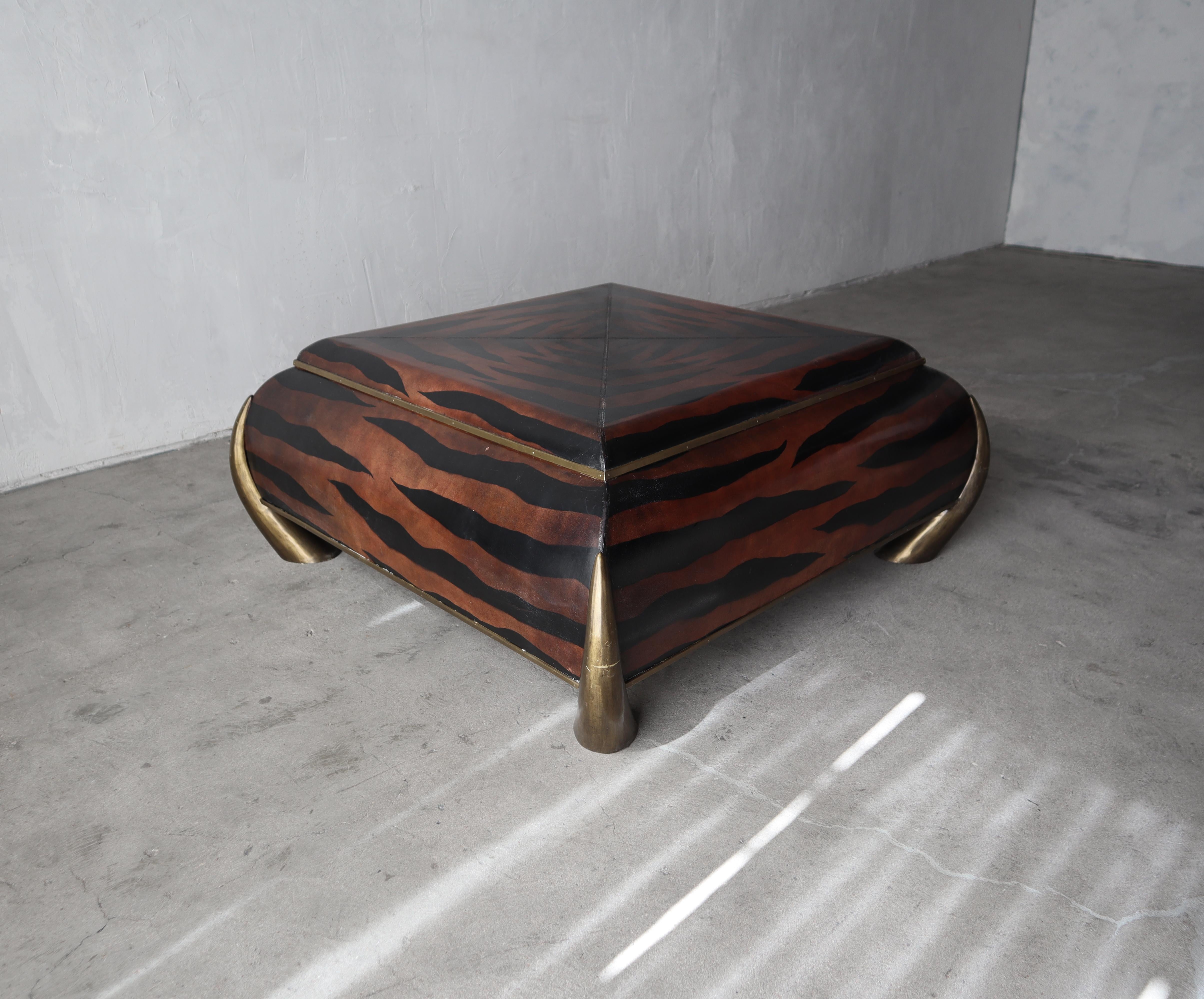 This gorgeous, leather covered coffee table is an exemplary example of Classic Maitland-Smith craftsmanship.

The coffee table is covered in leather with hand painted tiger striping, hand tooled details and super chunky, solid brass tusk legs.

The