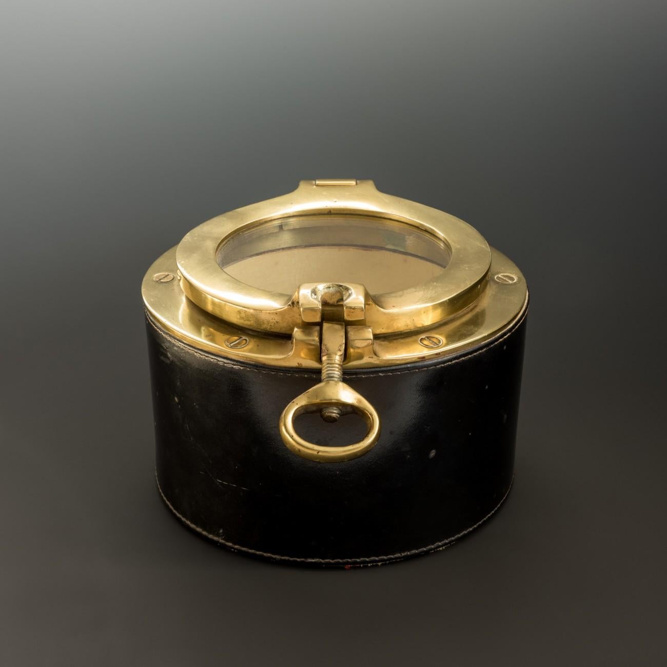 A stylish mid-20th century brass box modelled as a porthole with stitched leather covering, in the style of Jacques Adnet. Originally made for use as a tobacco jar, circa 1960.

Dimensions: 16.5 cm/6½ inches (diameter) x 10.5 cm/4? inches
