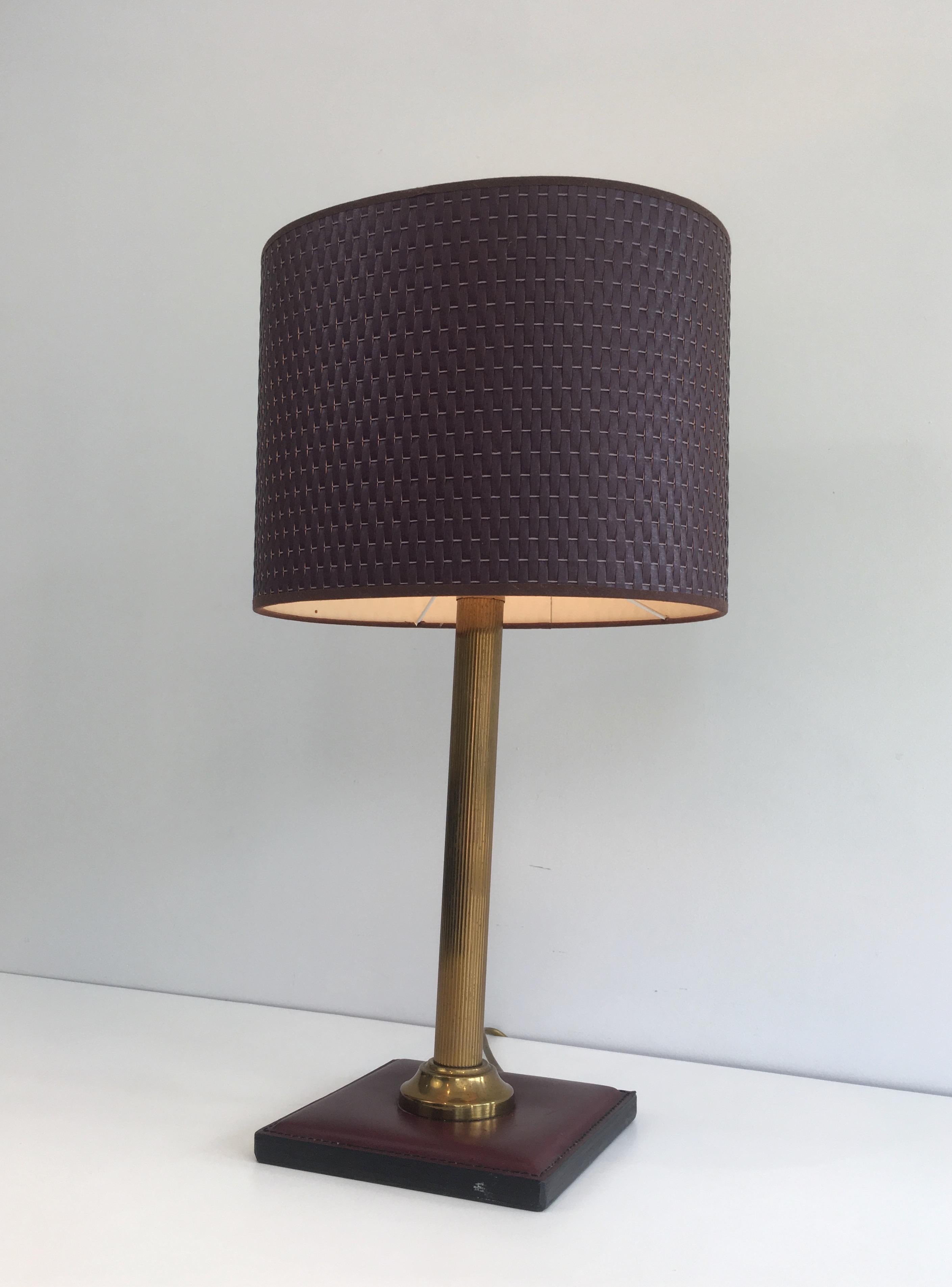 This table lamp is made of a burgundyish leather and brass. This lamp has an oval worked shade. This is a French work, circa 1970.