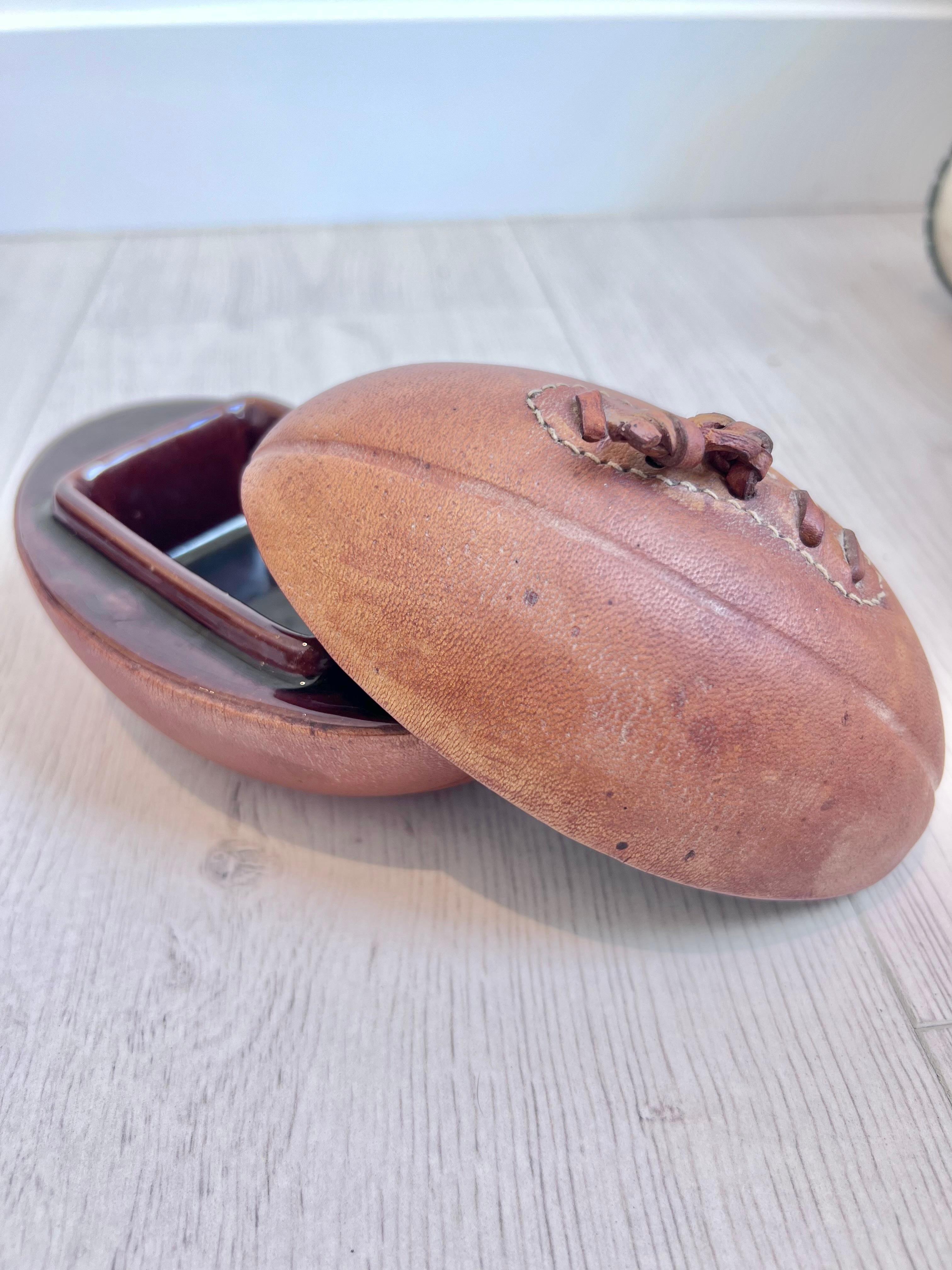 Handsome leather and ceramic ashtray/catchall by Longchamp in the design of an old football. Stamped with Lonchamp - France on the base. Beautiful patina to brown leather. Opens up to reveal the deep brown ceramic ashtray in flawless condition.