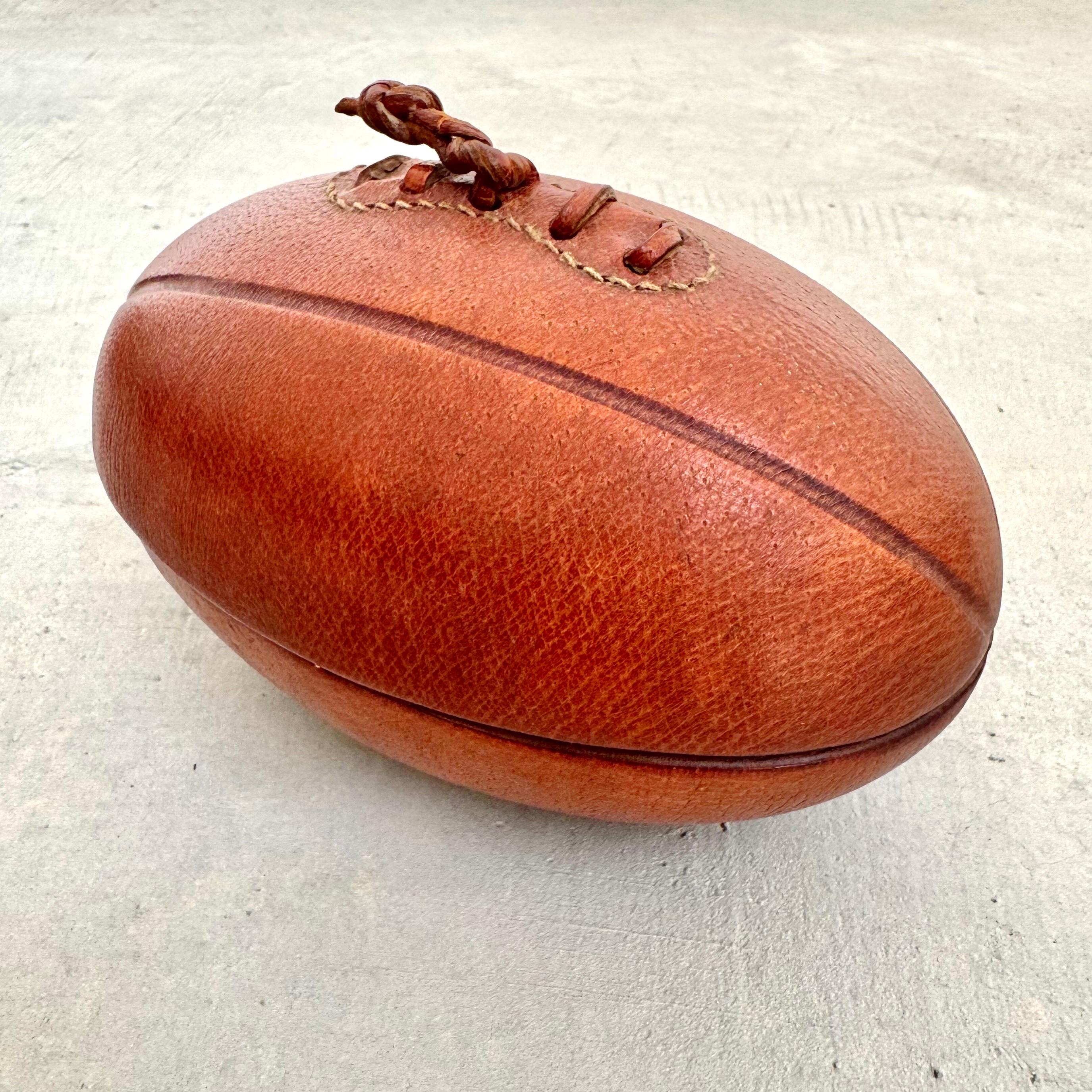 Joli cendrier/catalogue en cuir et céramique de Longchamp au design d'un vieux ballon de football. Estampillé Longchamp - France sur la base. Belle patine du cuir brun. S'ouvre pour révéler le cendrier en céramique brun foncé dans un état