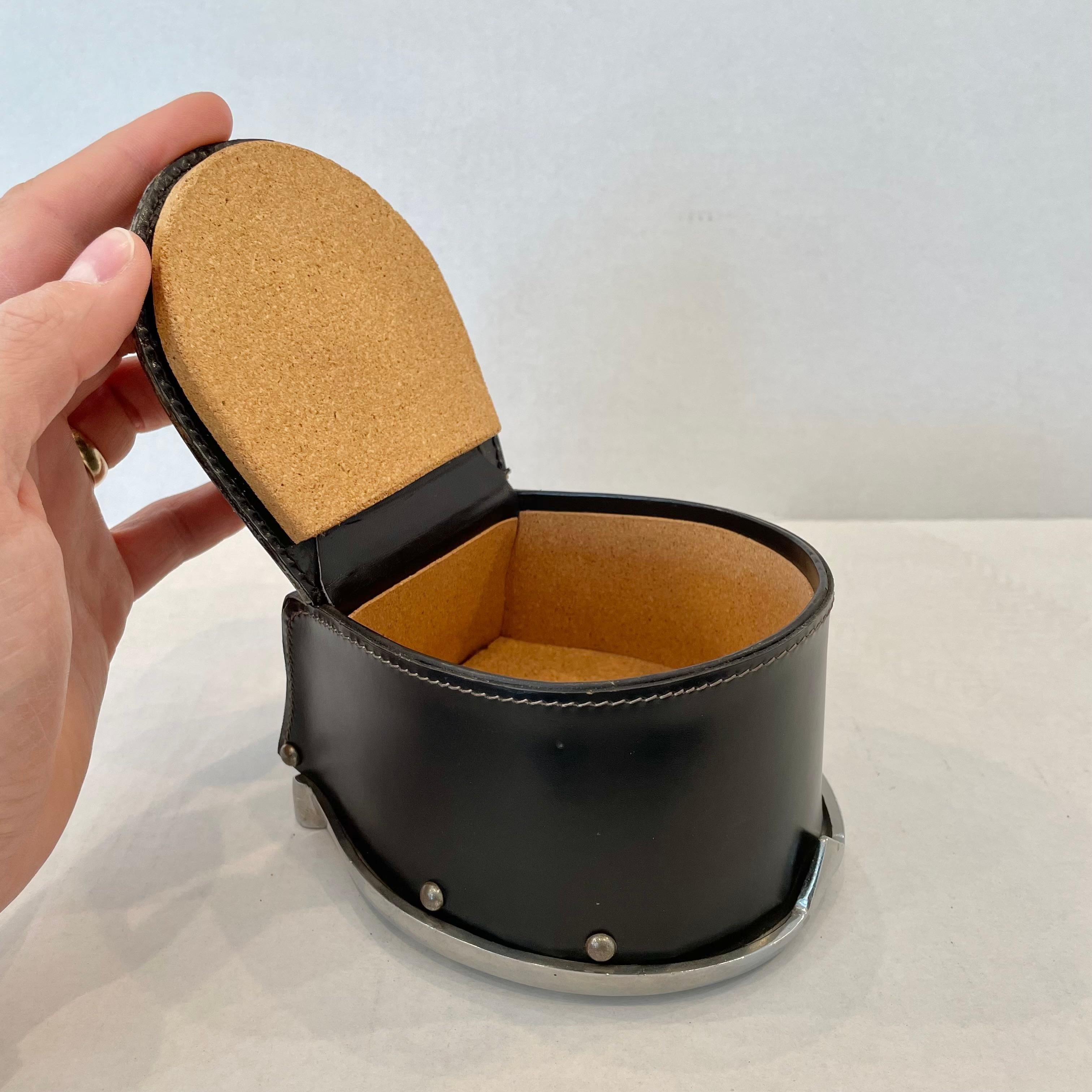 Handsome leather and cork tobacco box from France. Great scale and design. Beautiful metal horseshoe design is used as the base and a miniature metal pipe sculpture sits atop the lid as a handle. Box is completely wrapped in smooth black leather.