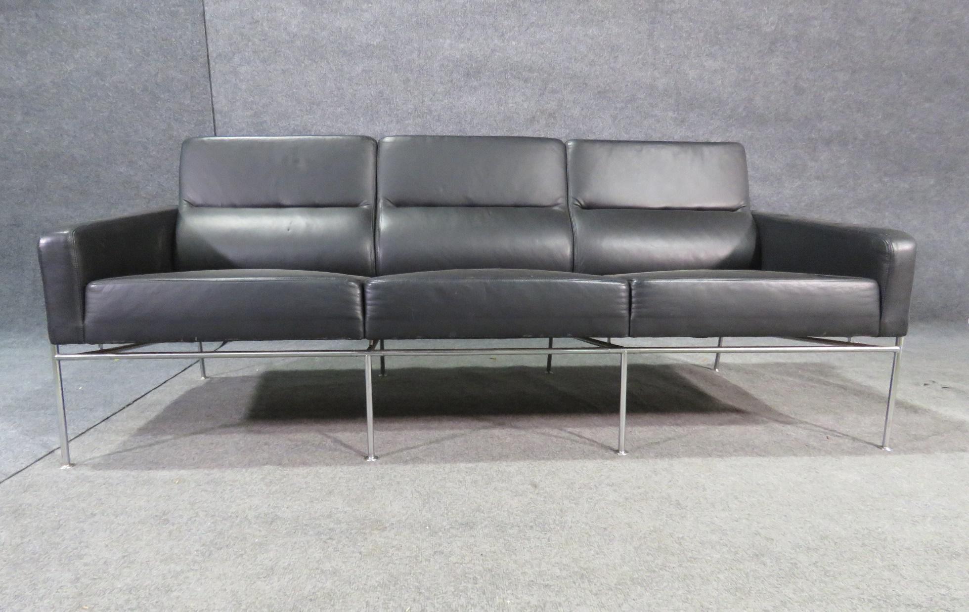 This Mid-Century Modern sofa, styled after the iconic designs of Arne Jacobsen, boasts a stylish simple construction paired with sleek black leather and chrome. Comfortable and easy to clean, this sofa is a practical, versatile, and sophisticated