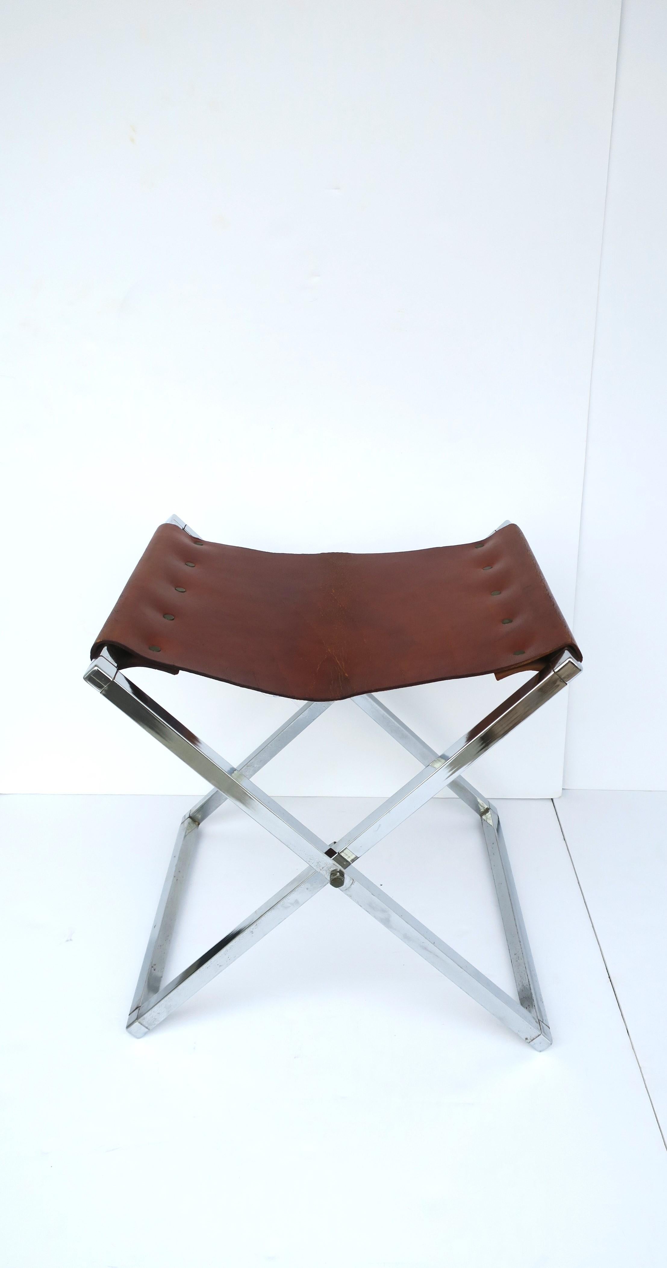 A well-made leather and chrome 'X' bench or stool, in the campaign modern style, circa 1970s. Stool/bench seat has a brown leather top (brown leather with red-ish undertones), brass detail and an 'X' chrome frame. Frame is a niece weight. Great as a