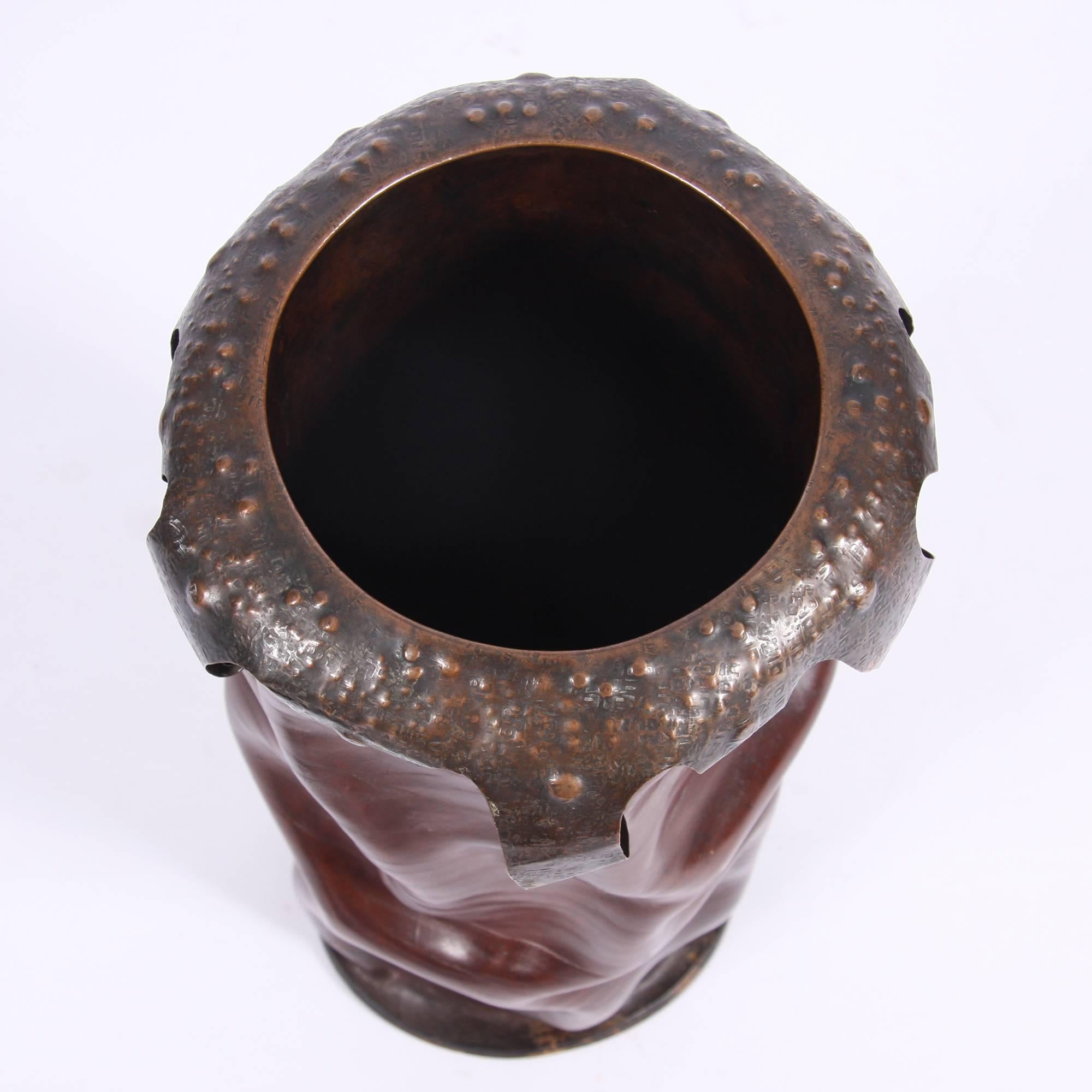 A leather and beaten copper umbrella stand, with a decorative trim. Darker leather. The surreal design makes the stand appear as if it's melting.