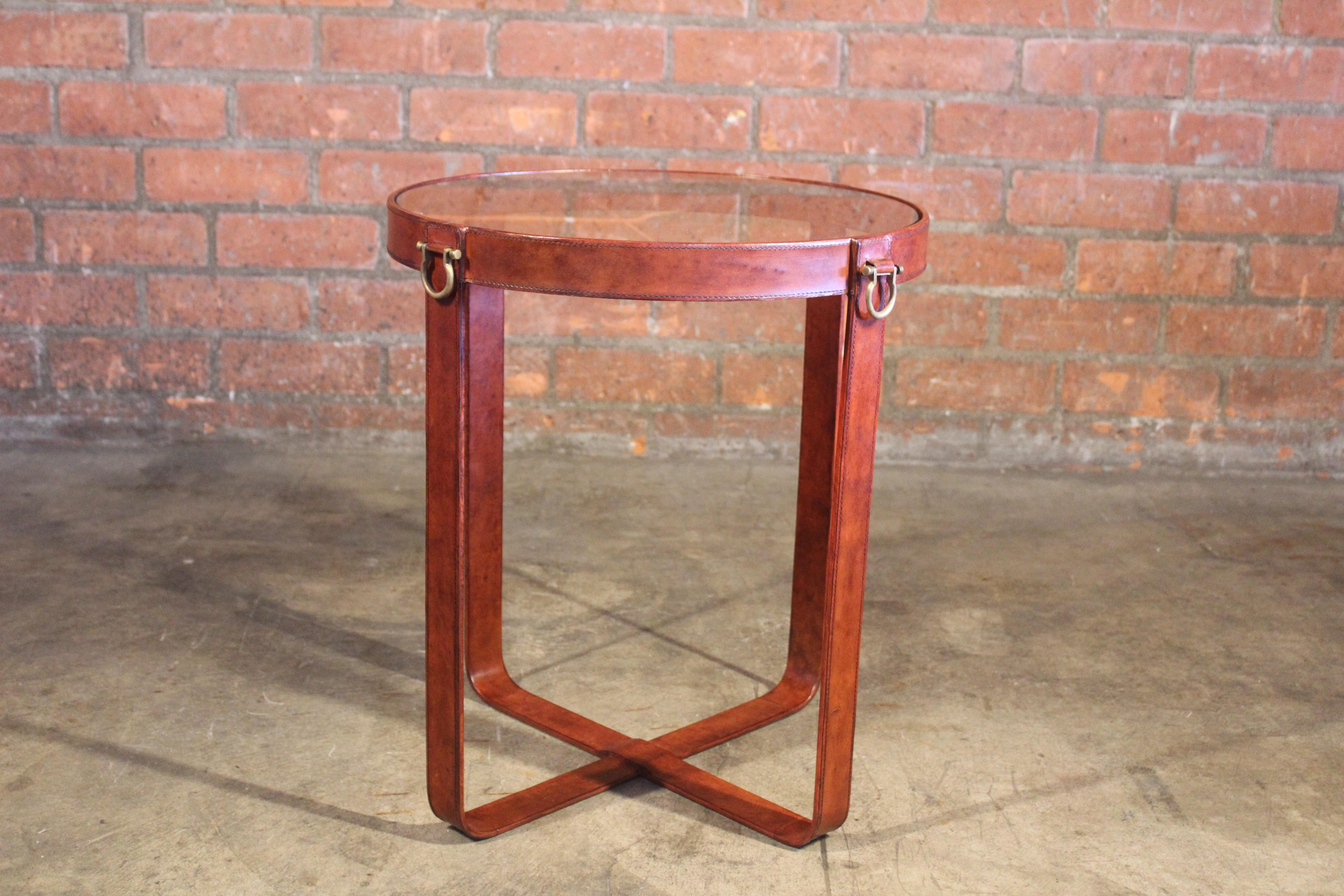 A leather wrapped side table with a reflective glass surface and brass hook details. In good condition. In the style of Jacques Adnet.
