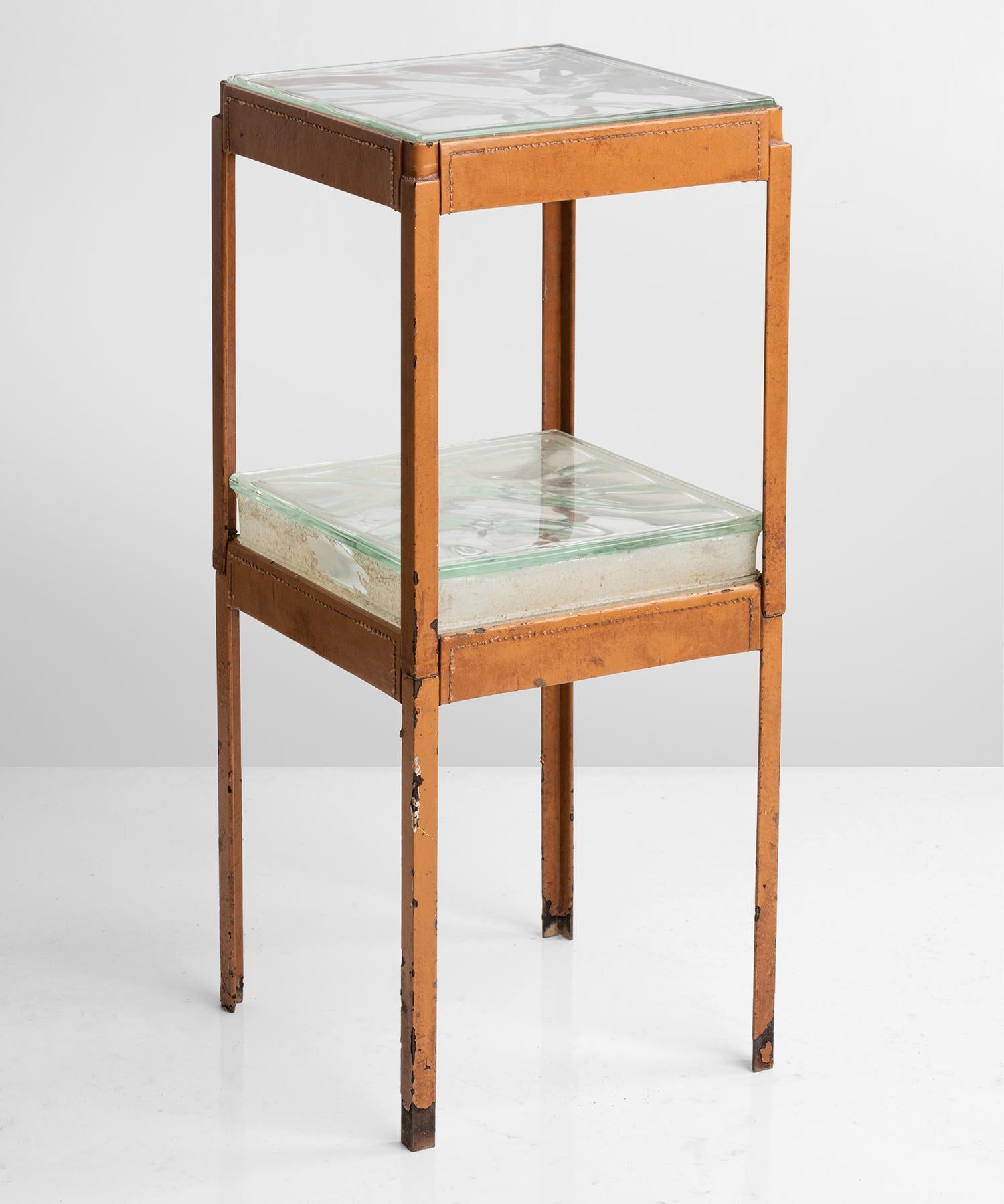 Metamorphic metal side table bound in leather with thick glass surface.