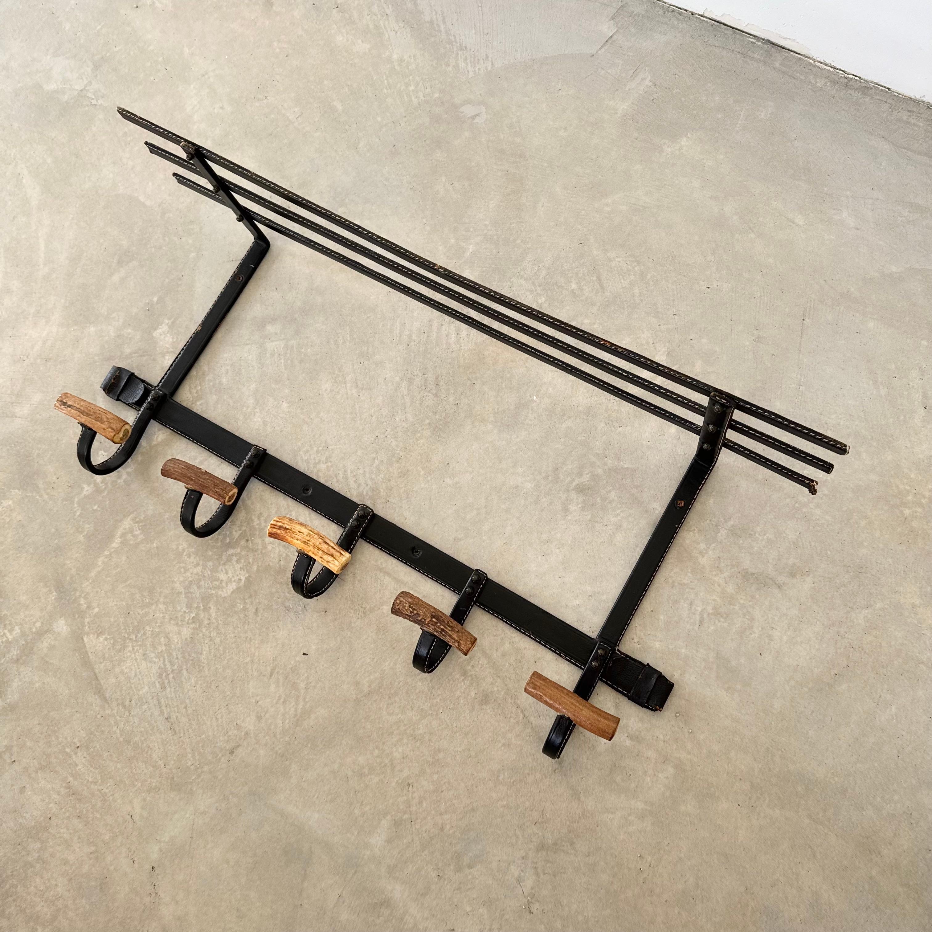 A handsome, spacious coat rack by French designer Jacques Adnet. The black iron frames are completely wrapped in black leather, featuring Adnet's signature contrast stitching. Three bars across top provide ample shelving space. Each of the 5 hooks