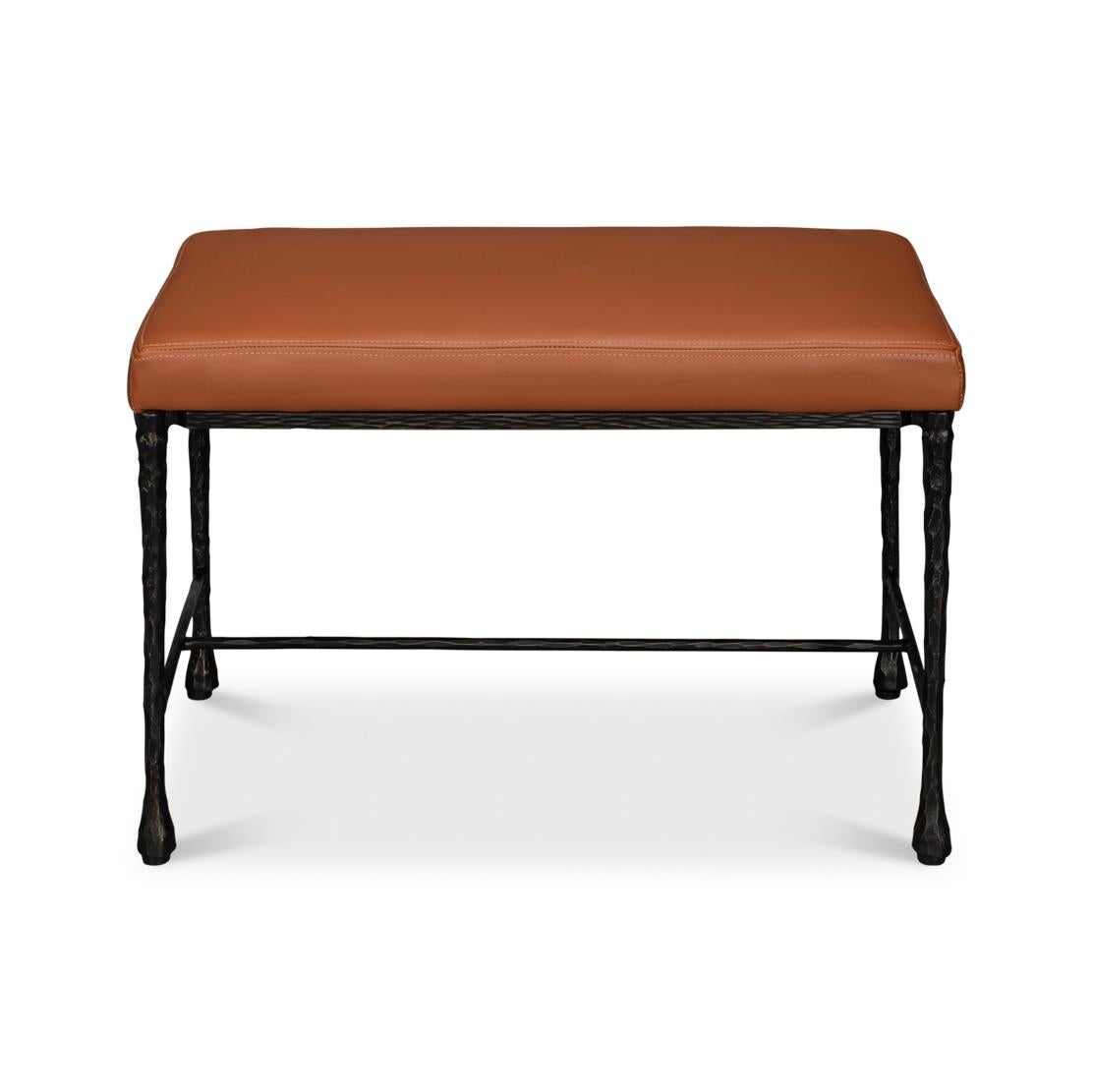 Sa base robuste en fer forgé à la main présente une finition texturée et des pieds effilés, mettant en valeur un authentique design artisanal. Dotée d'une assise en cuir moelleux brun caramel, cette banquette offre à la fois confort et