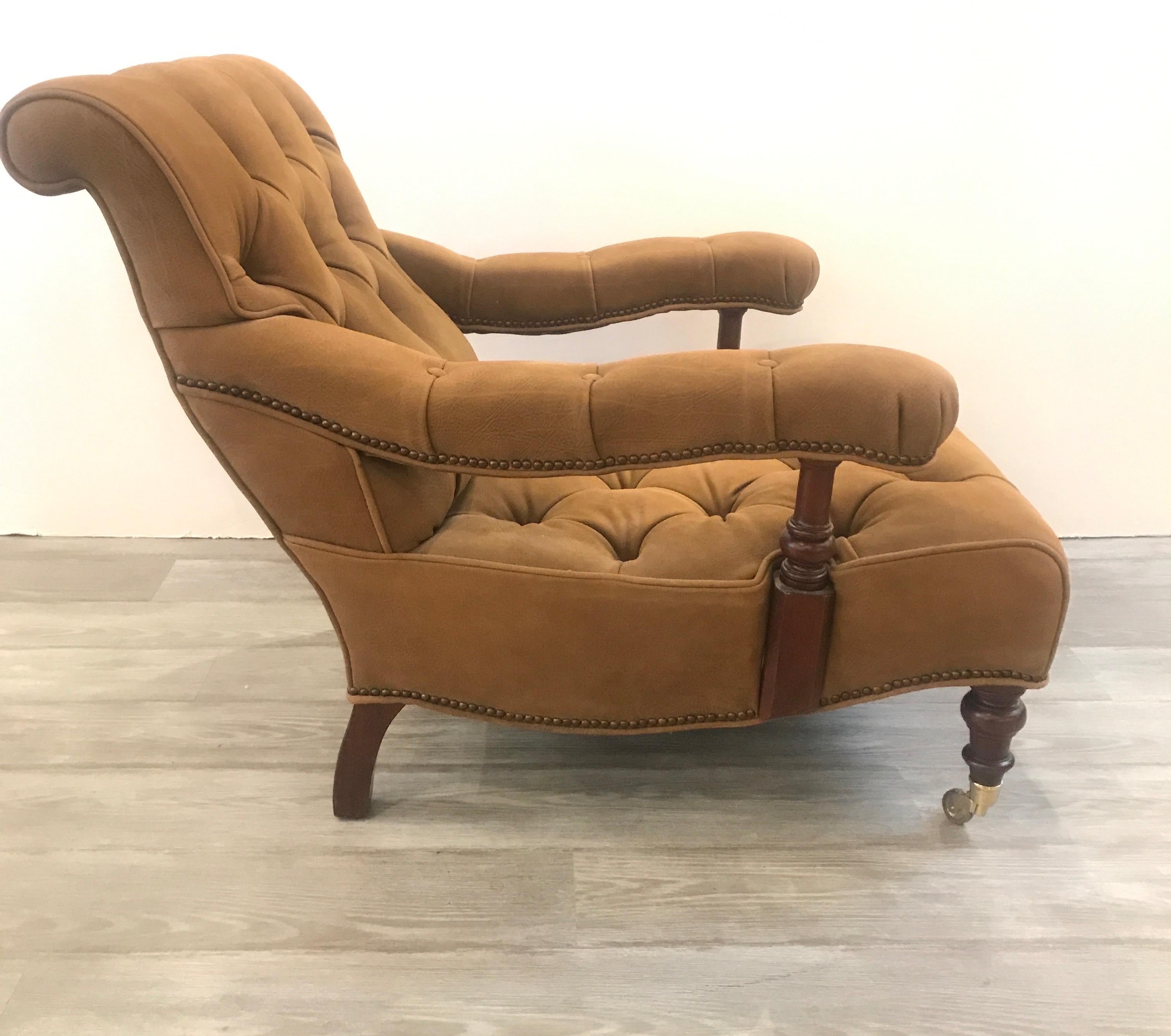 A leather and mahogany framed lounge chair. The chair with brass nailhead trim and tufted seat and back. The silhouette is lower and very comfortable. The leather is more of a buckskin without the shiny finish of polished leather. The style is from