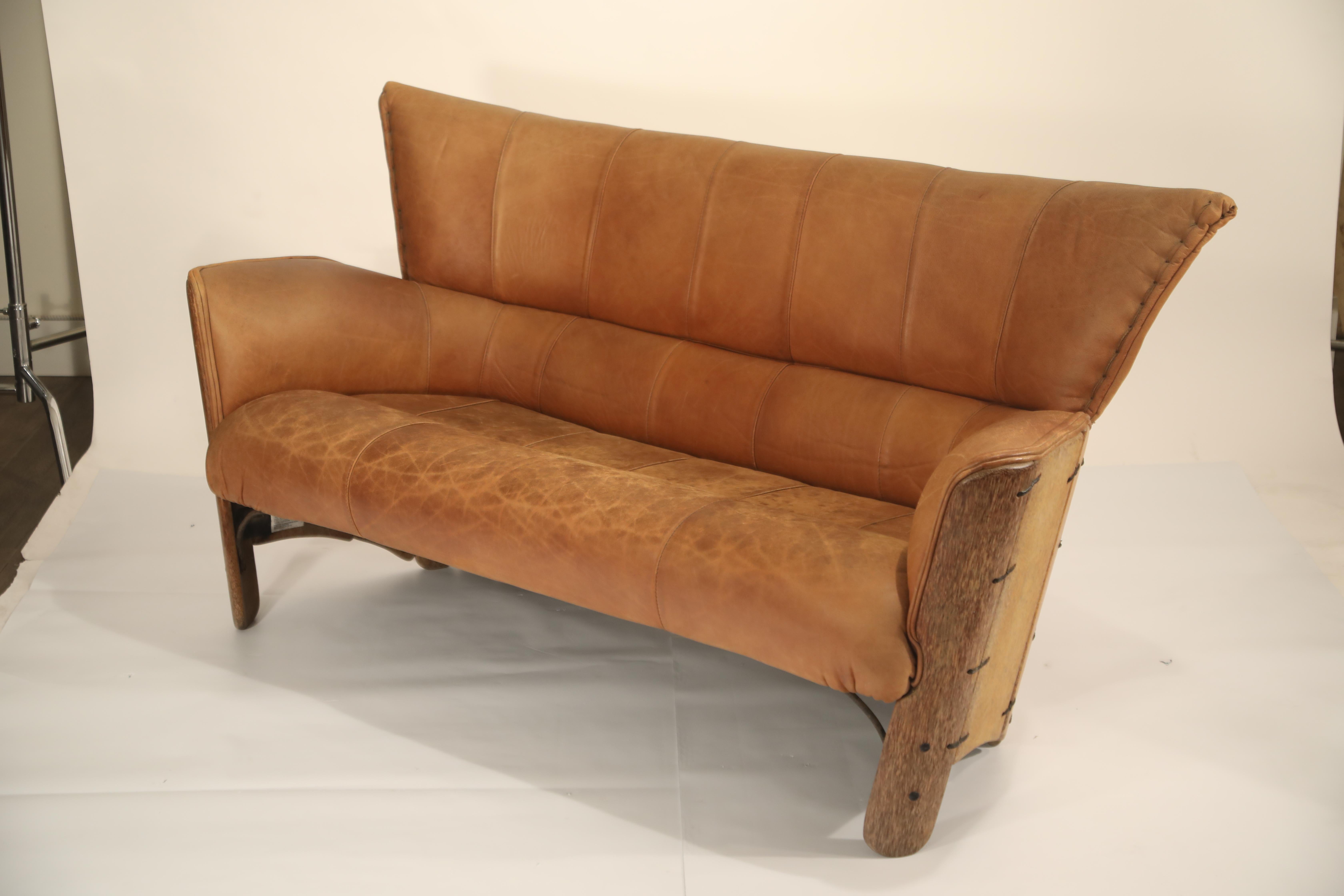 This incredible lightly distressed leather and palmwood sofa by Pacific Green is the perfect designer piece that can both stand out in a space and feel right at home. It's unique wingback styling gives it a dramatic look, while the light patina on