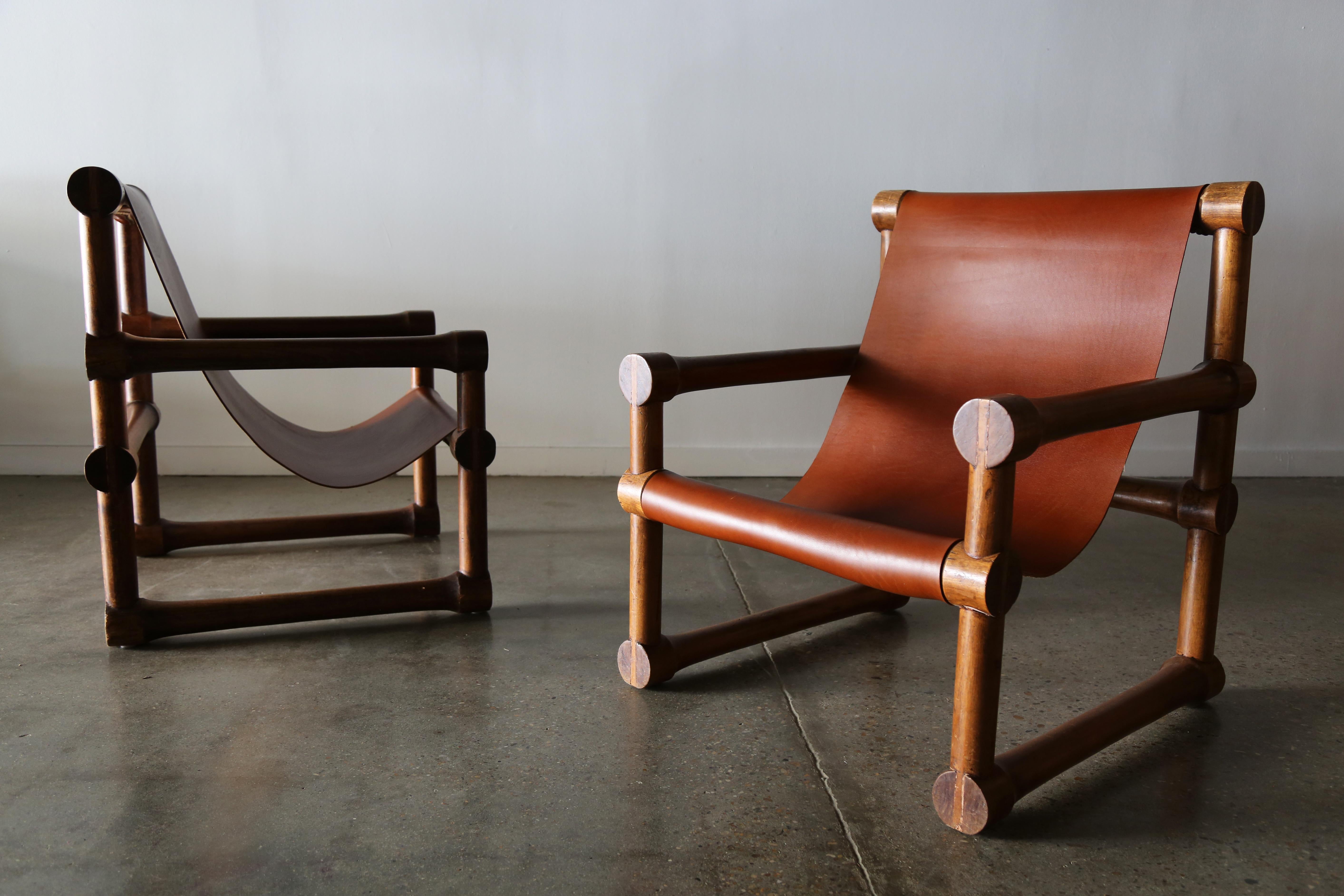 A utilitarian design consisting of thick saddle leather and what appears to be exotic hardwood construction. This pair of chairs feature a log cabinesque, stacked and joined solid wood construction which yields to the seemingly paper thin leather