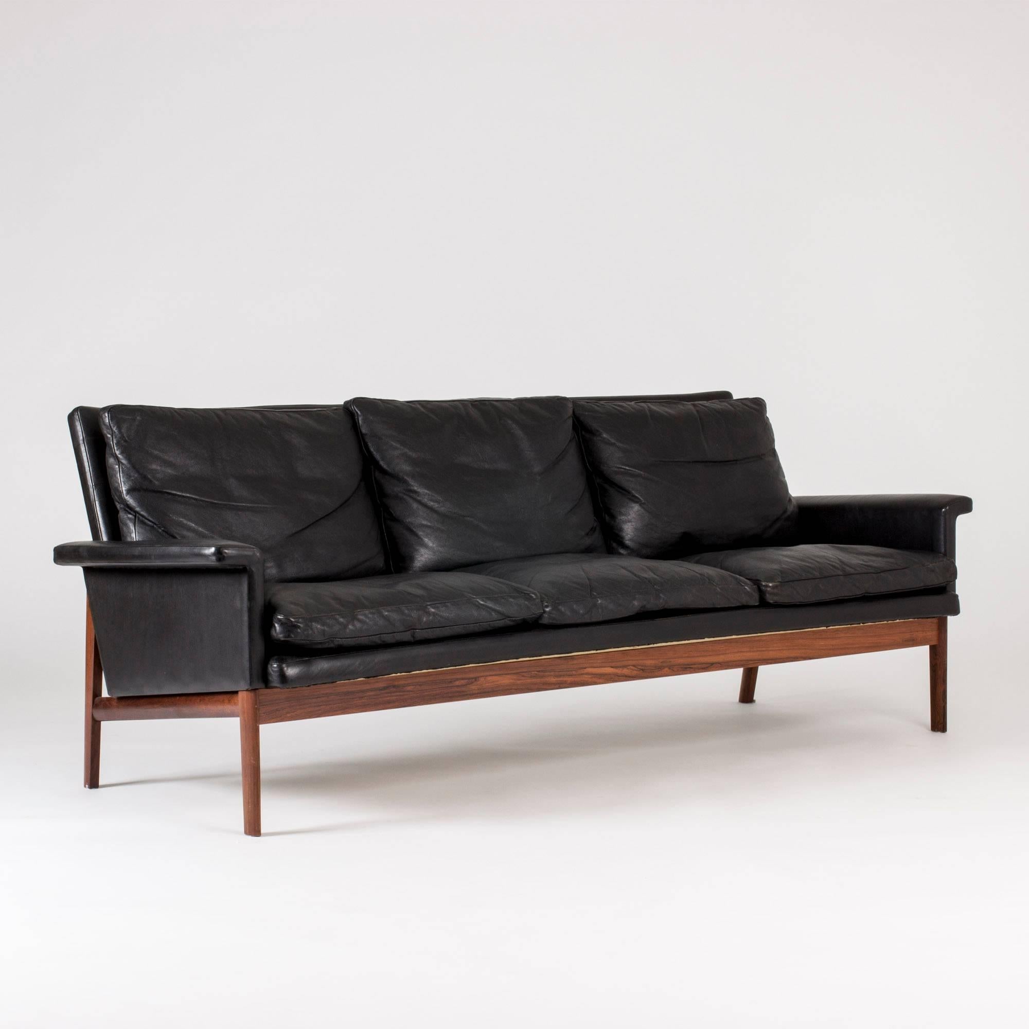 Black leather and rosewood three-seat “Jupiter” sofa by Finn Juhl. Nice lines and subtle details such as the ever so slightly curved backrest and elliptic legs that appear wide or slender depending on angle. Leather in very good condition.