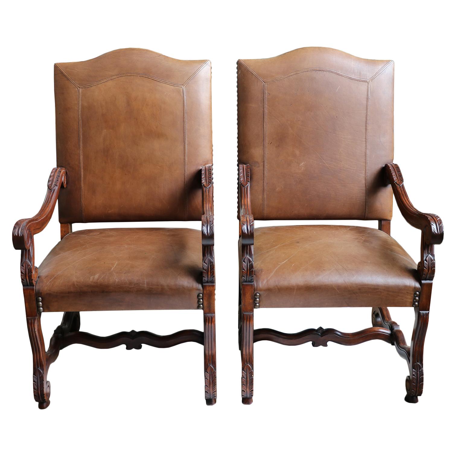 Pair of sturdy leather arm chairs with nail head and carving details. Note, the wear in the seating area and the pre-owned conditions.