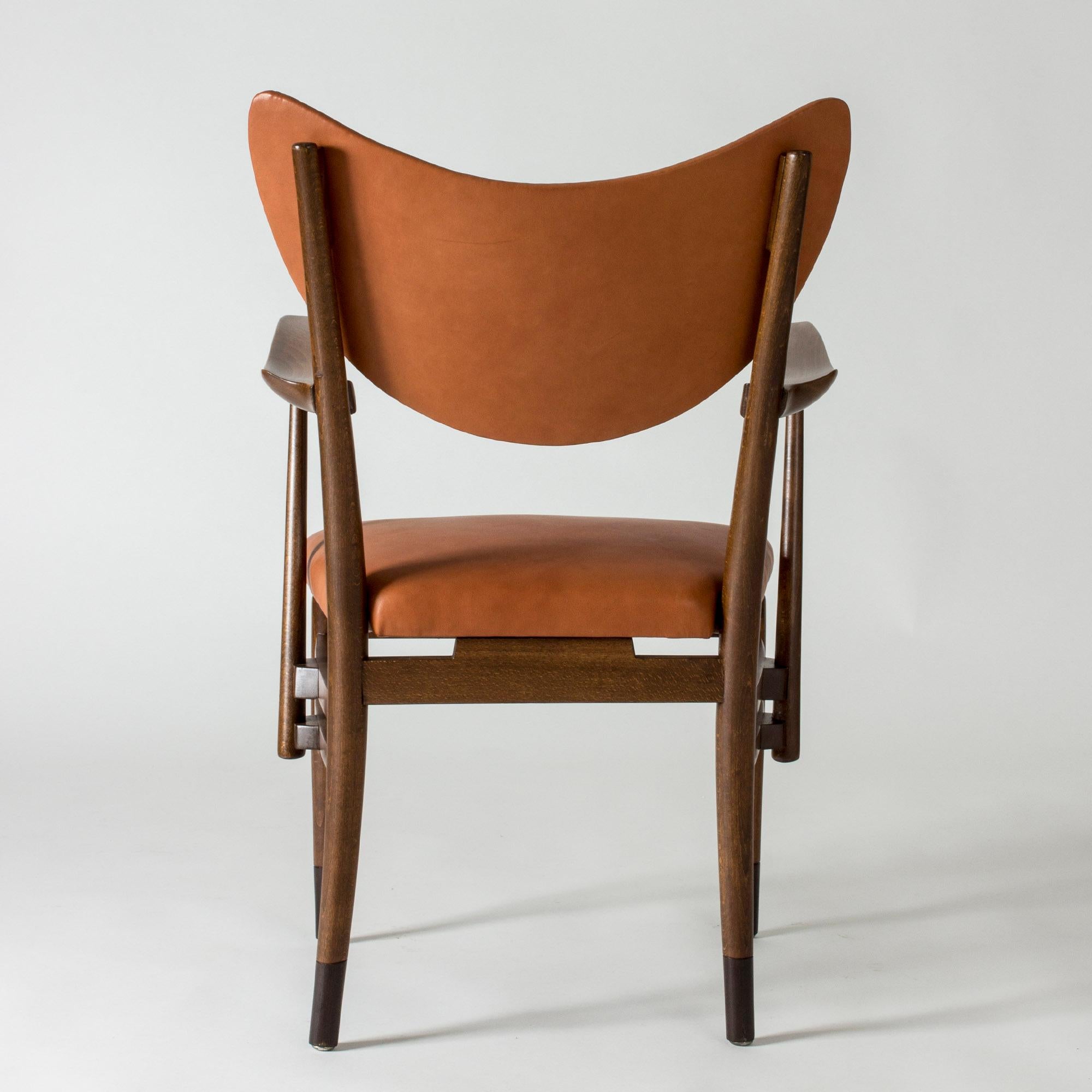 Cool and elegant armchair, attributed to Eva and Nils Koppel. Stained wooden frame with sculpted armrests, boldly curved backrest. Seat and back dressed with supple cognac brown leather.