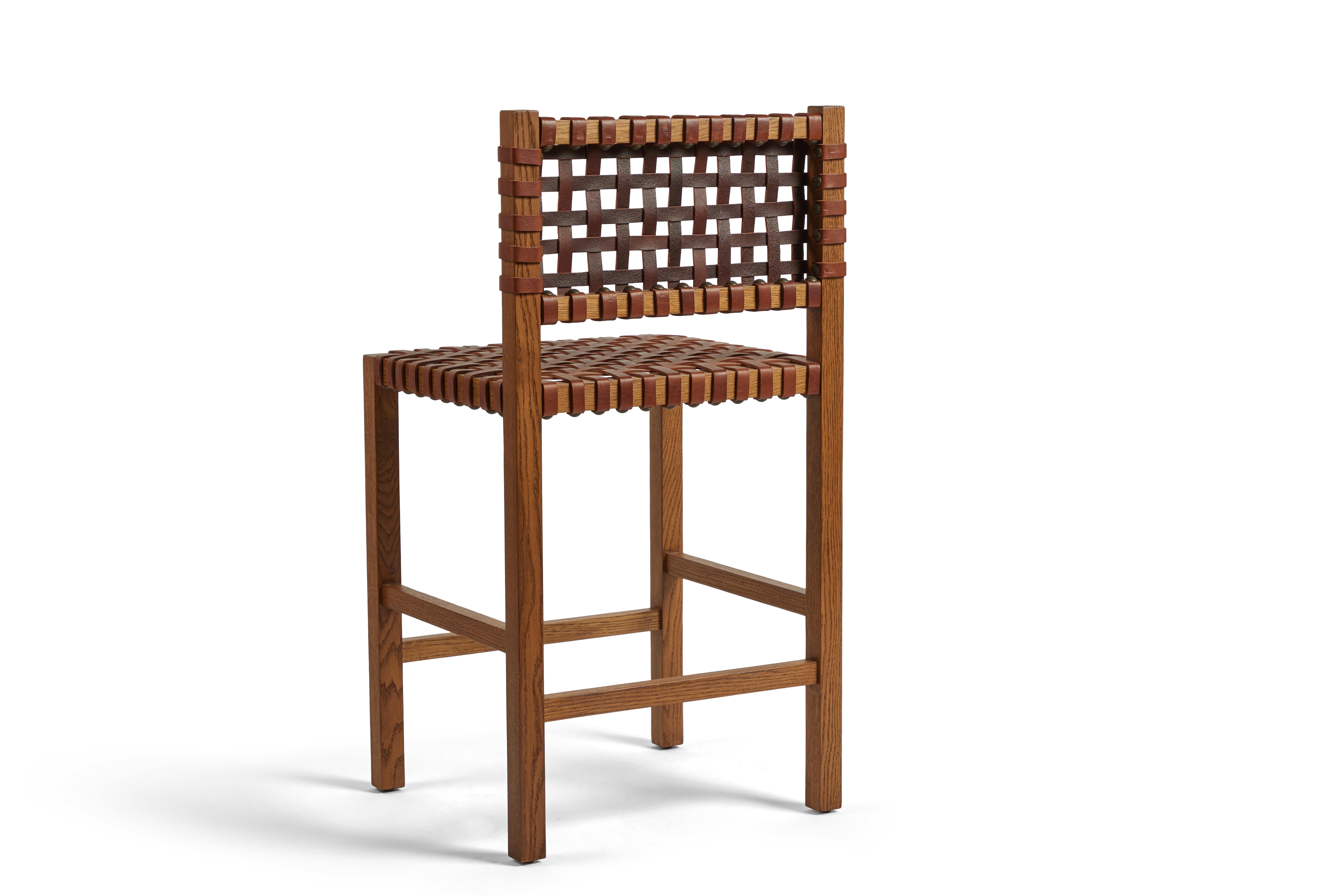Questi sgabelli da banco rialzati sono la nostra rivisitazione moderna di un tradizionale sgabello da bar in pelle. Presenta una finitura in quercia bianca tinta, seduta e schienale in pelle intrecciata e teste di chiodi in bronzo. 
