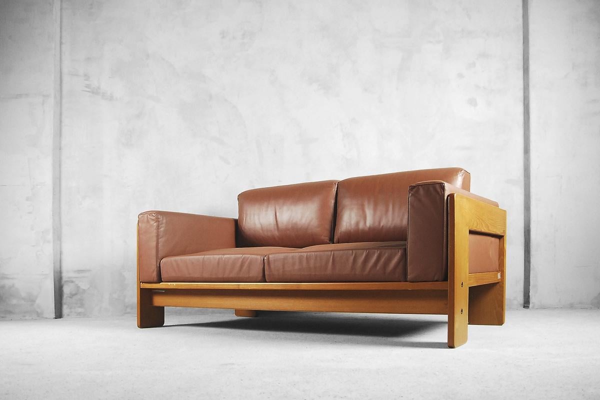 This wide and grand example of the Bastiano sofa is designed by Tobia & Afra Scarpa in 1962 and produced by KnollStudio. The two-seater sofa features thick sienna brown leather. The basket frame is made from stained wood, which displays a beautiful