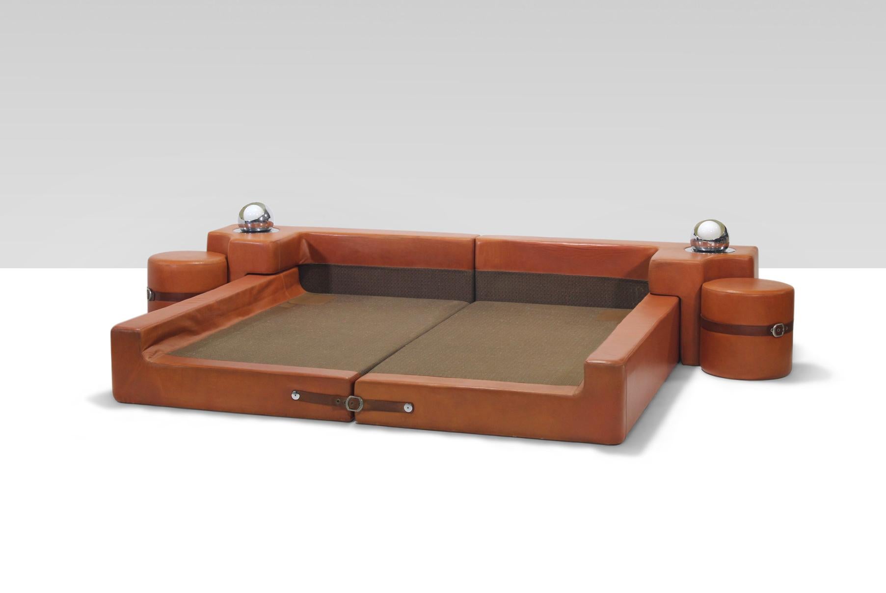 Cognac leather bed by Guido Faleschini for Mariani of Italy, circa 1975. This bed includes bed platform, headboard with built in reading lights, and round end tables/stools. The pieces of the bed are held together by leather belts and buckles. In
