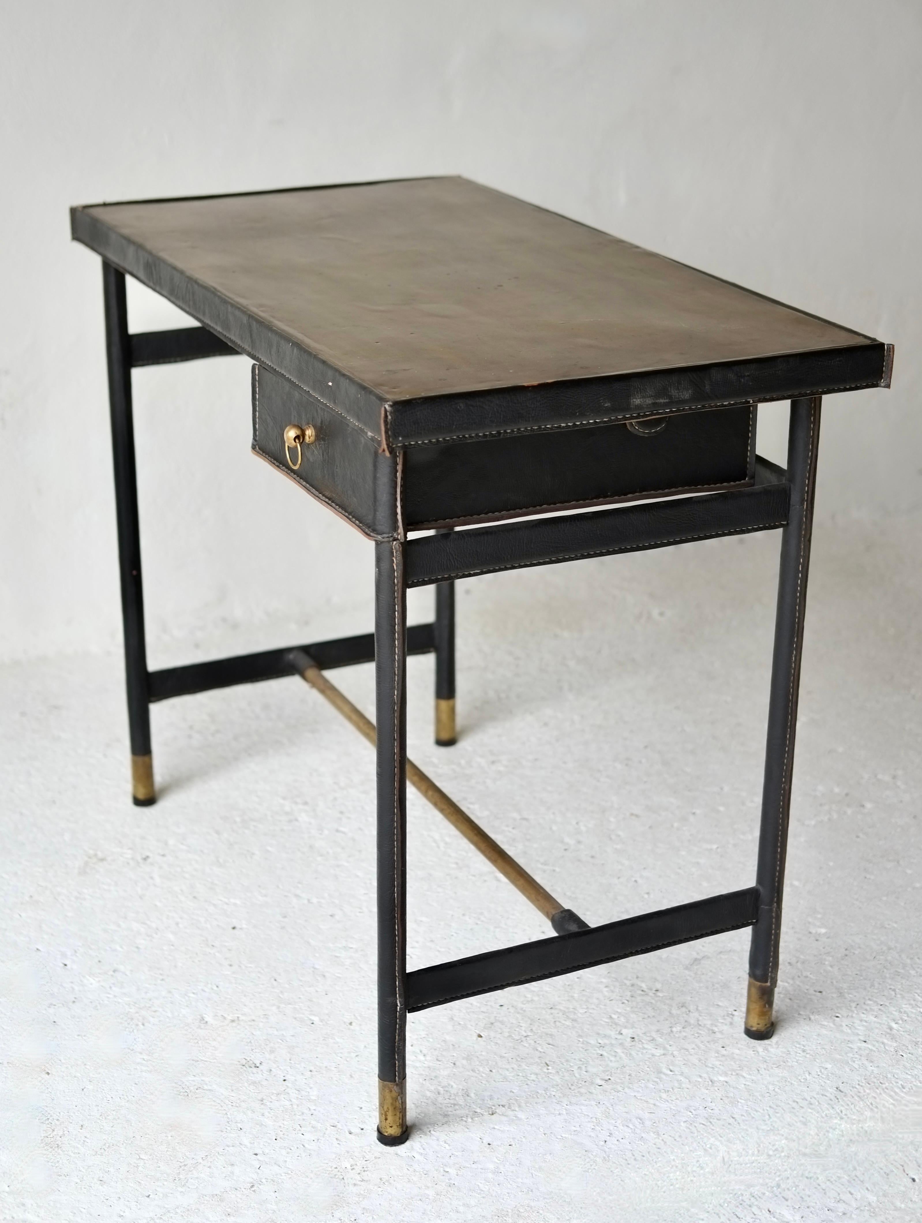 An elegant leather-clad desk with brass top and detailing, attributed to Jacques Adnet, France.

The design features two discreet drawers that pivot outward, exemplifying Adnet’s signature blend of functionality and refined modernism.

H 77 W 92 D